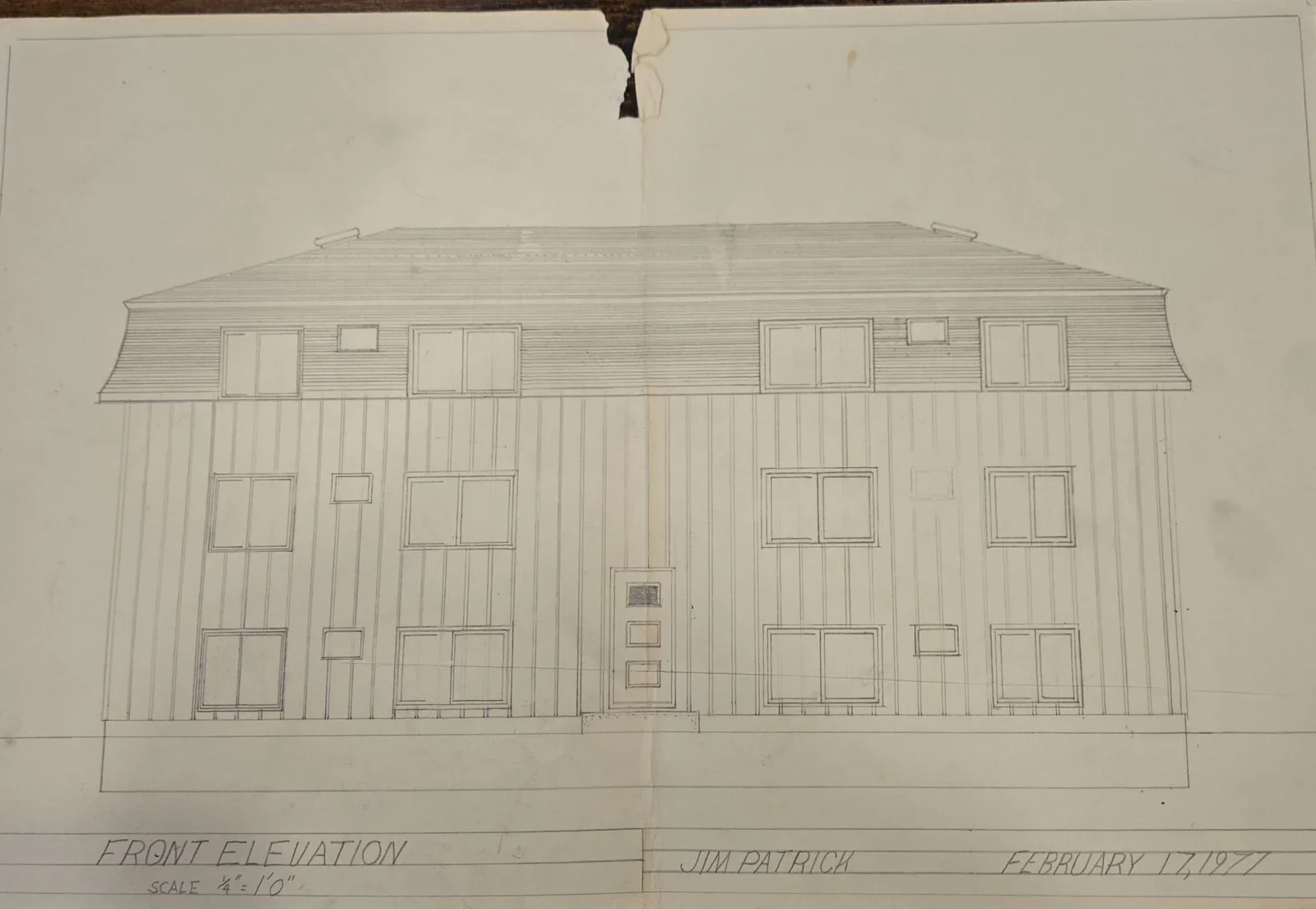 Architectural drawing of a three-story house with a pitched roof, multiple windows, and a central doorway, labeled 'Front Elevation, Jim Patrick, February 11, 1977'.