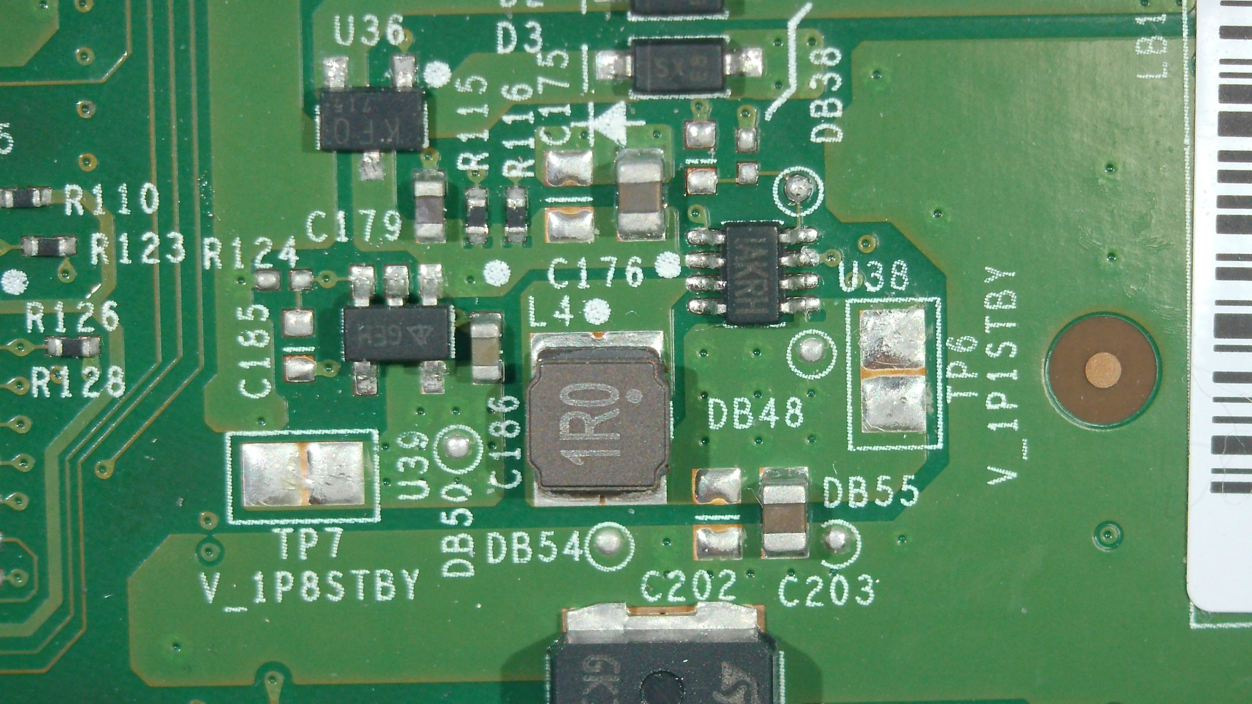 Close-up of a green printed circuit board with various electronic components, including resistors, capacitors, and integrated circuits, and white printed labels.