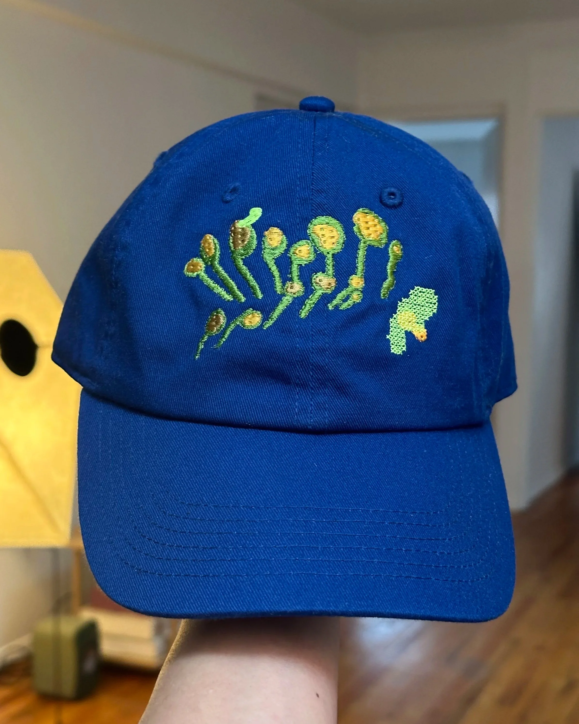 A person wearing a blue baseball cap with embroidered green and yellow flowers.