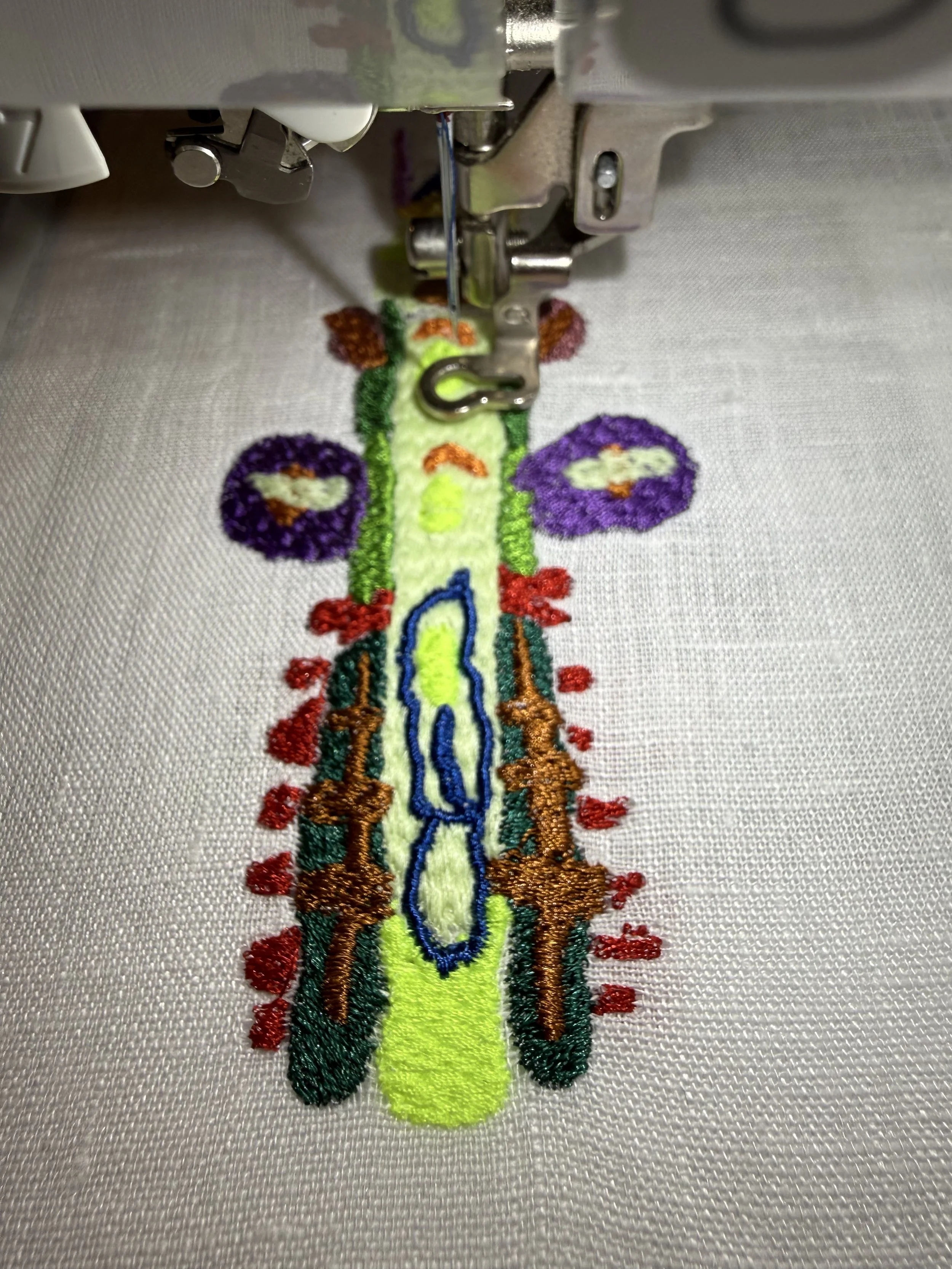 Close-up of embroidery machine stitching a colorful design of a caterpillar on white fabric.