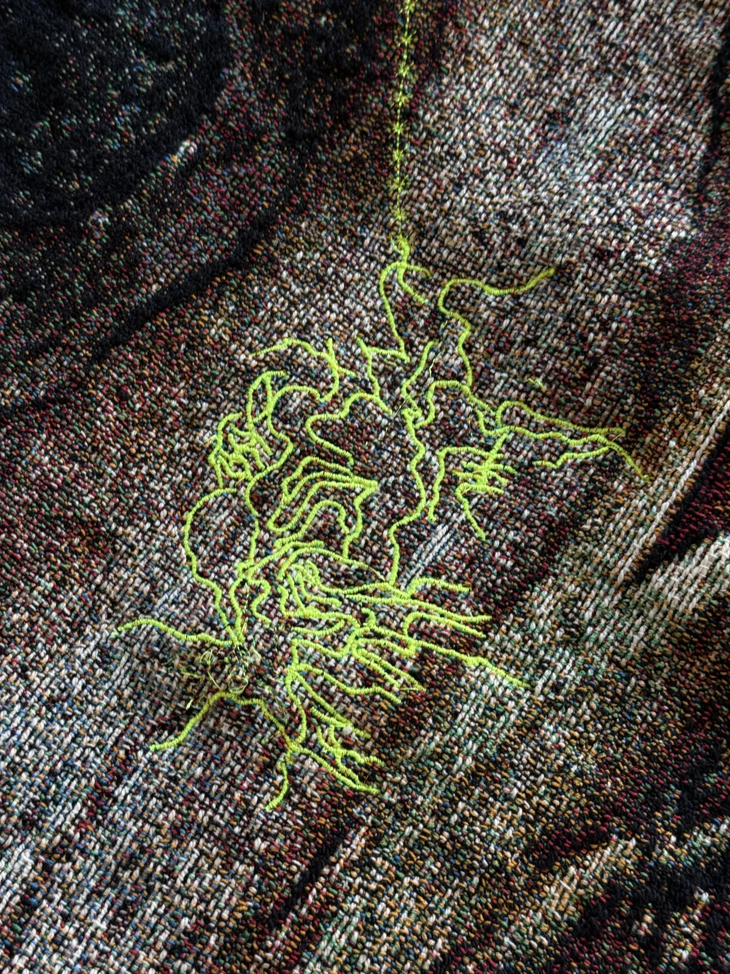 Close-up of a multicolored woven textile with embroidered green designs.