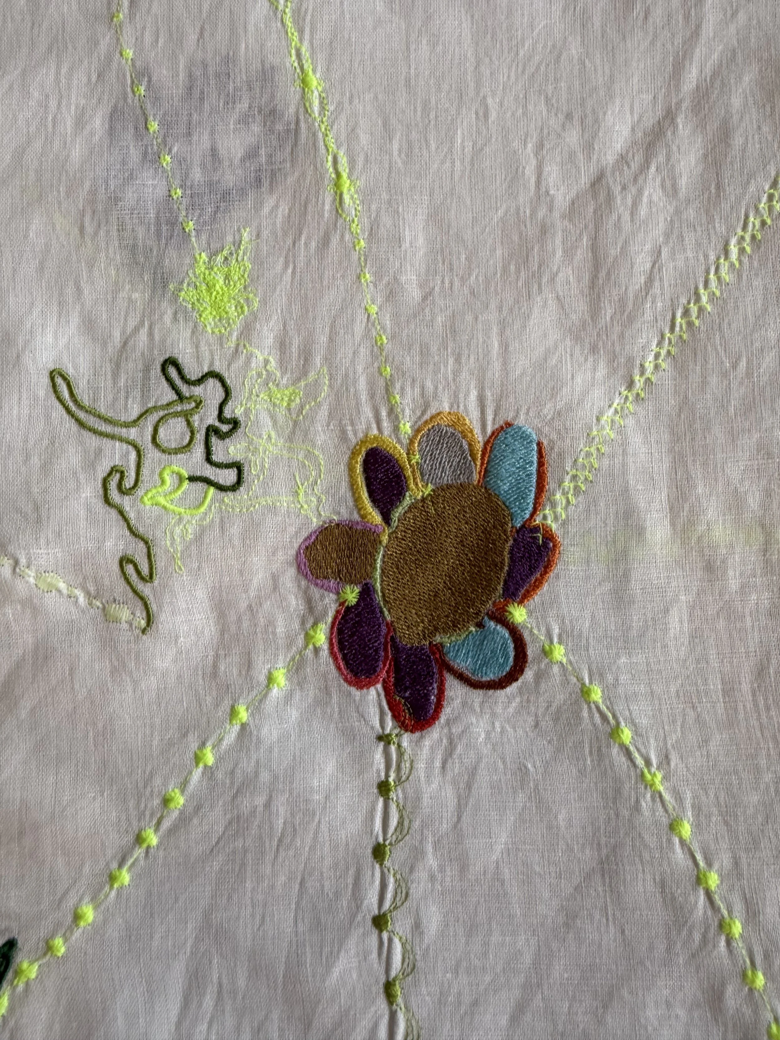 Colorful embroidered flower with stitched leaves on a textured fabric background.