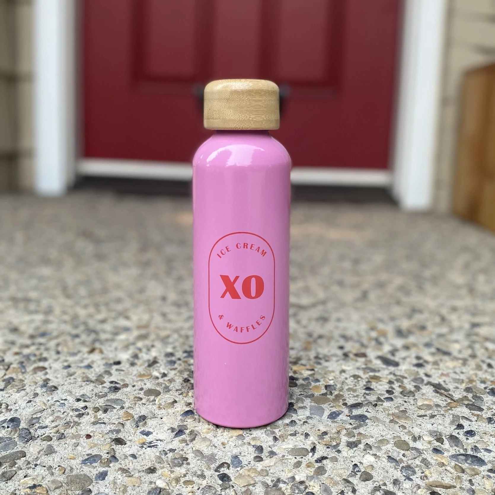 Cute pink metal water bottle with wooden top and XO logo on a front porch