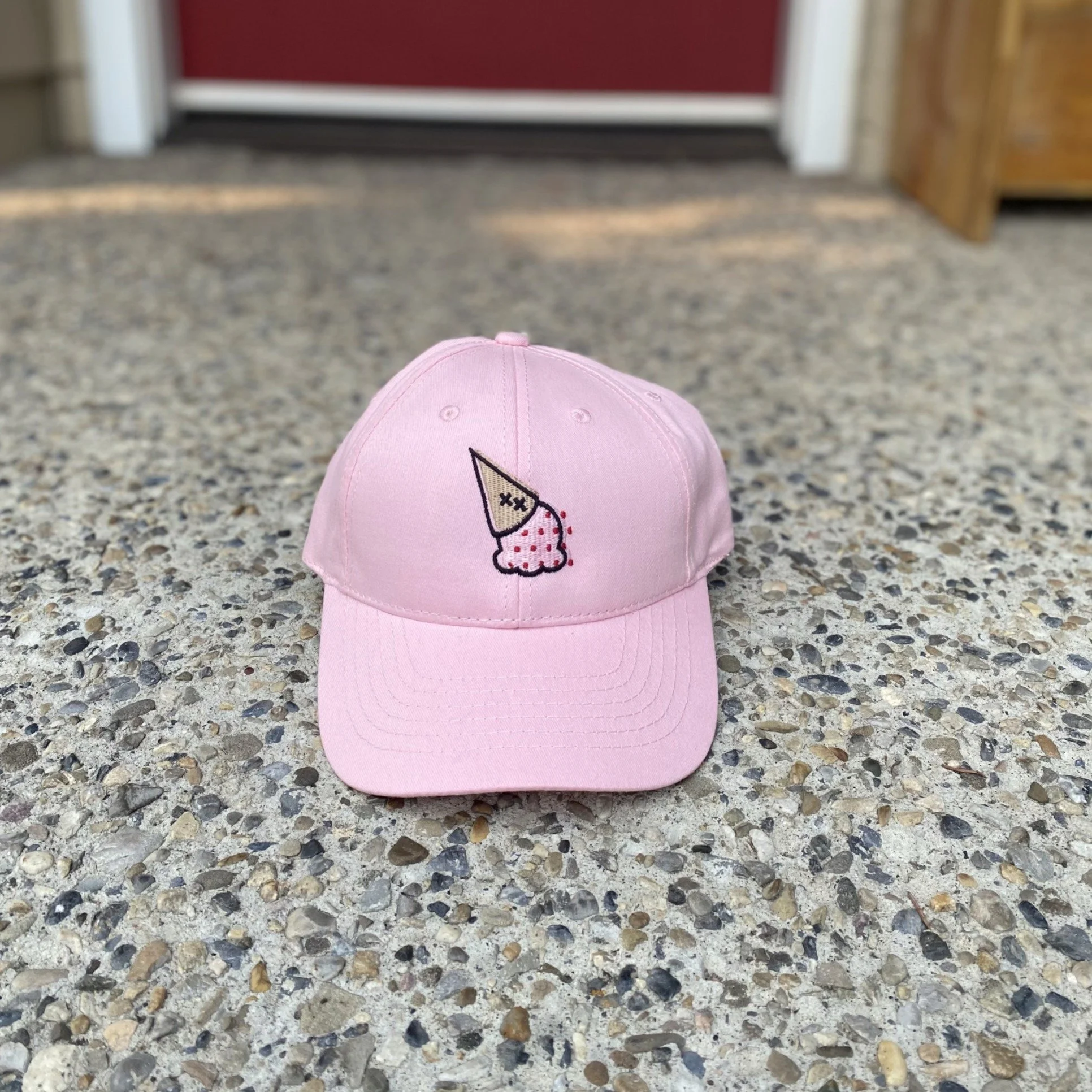 Pink ball cap with XO upside down cone logomark embroidered, on a front porch