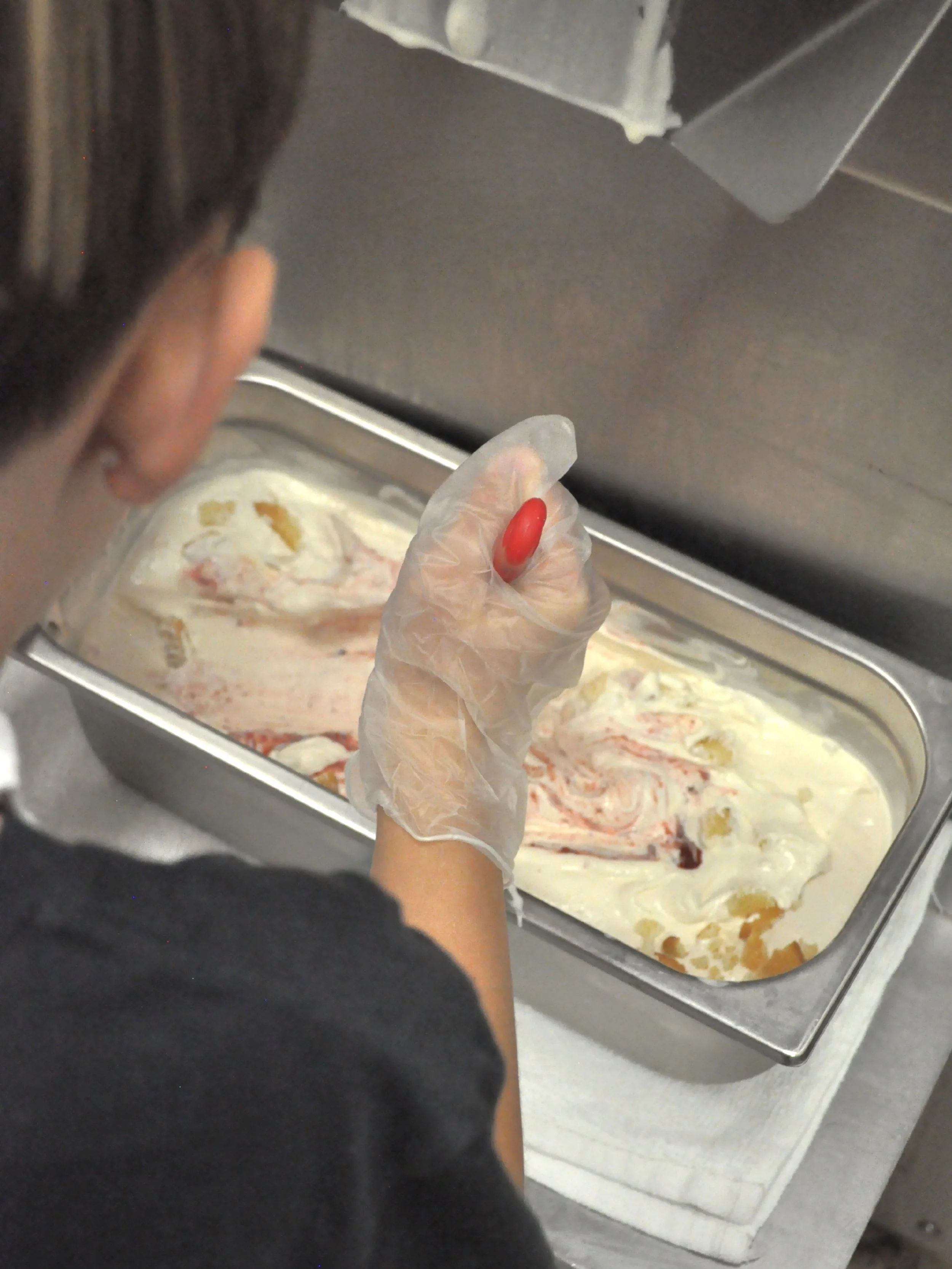 A child wearing a glove is swirling strawberry jam in the ice cream he just made.