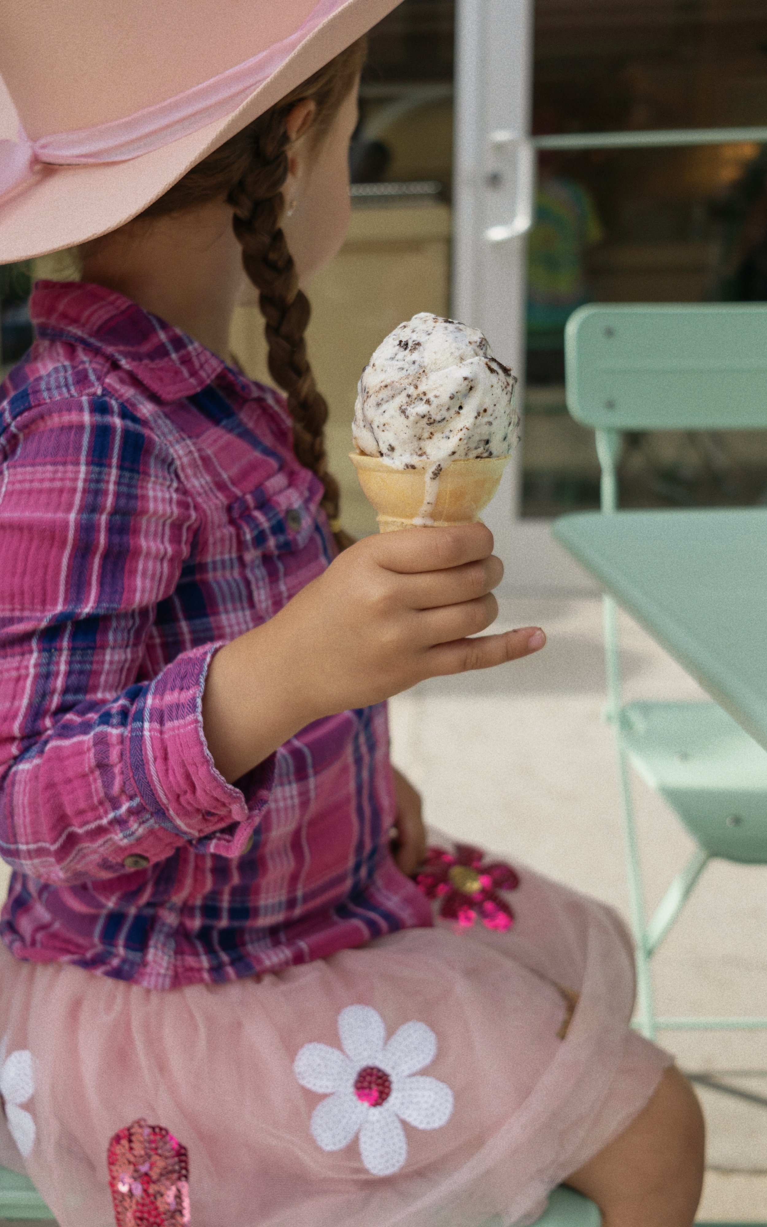 Child dressed in pink eating an ice cream cone that's melting on her fingers