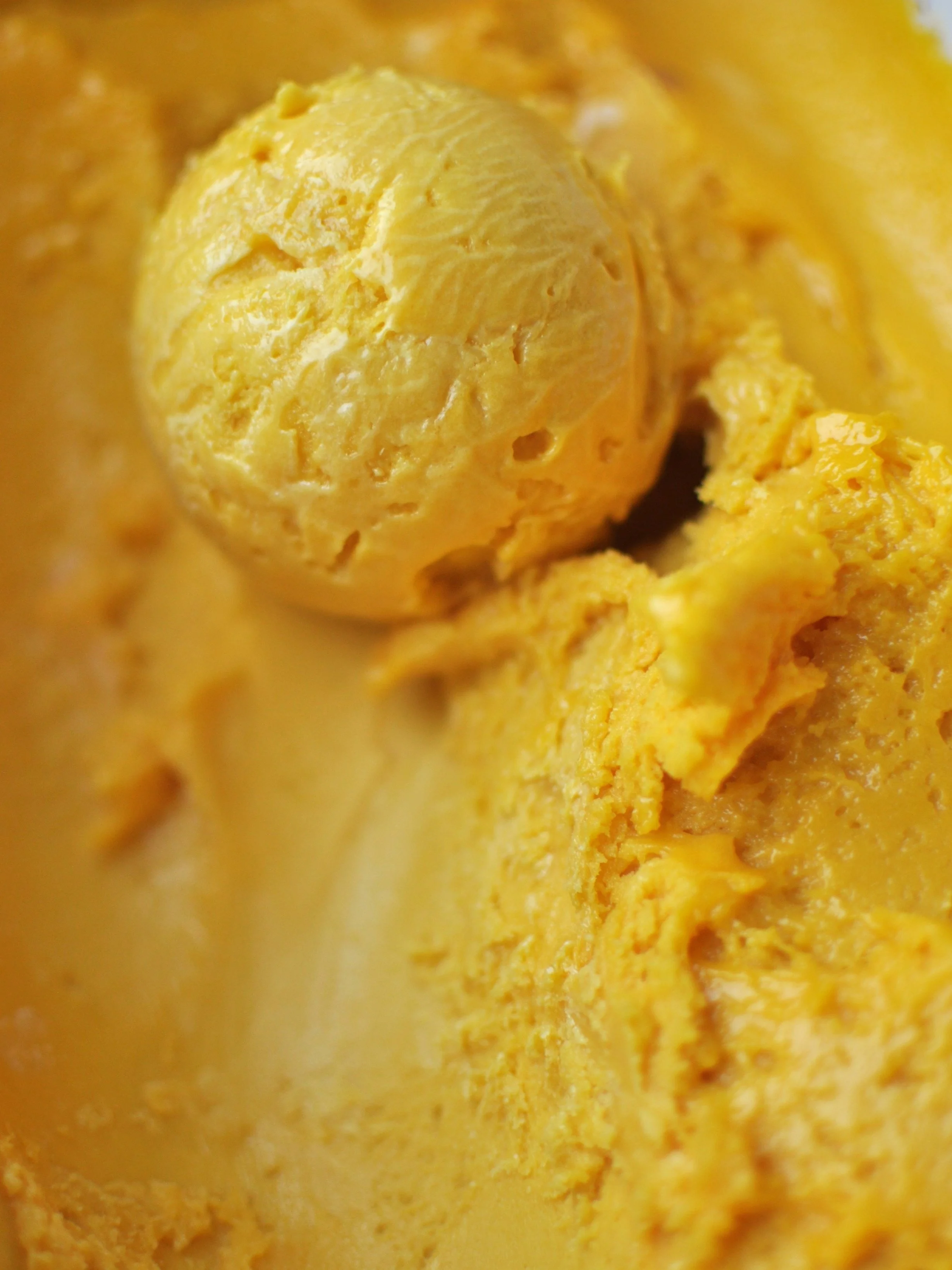 Close up of a bright yellow scoop of Mango sorbet.