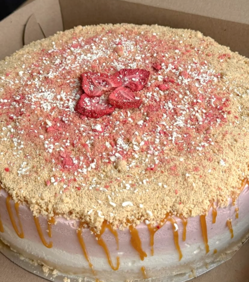 Strawberry vanilla ice cream cake topped with a crumbly topping, strawberry slices and caramel drizzle.