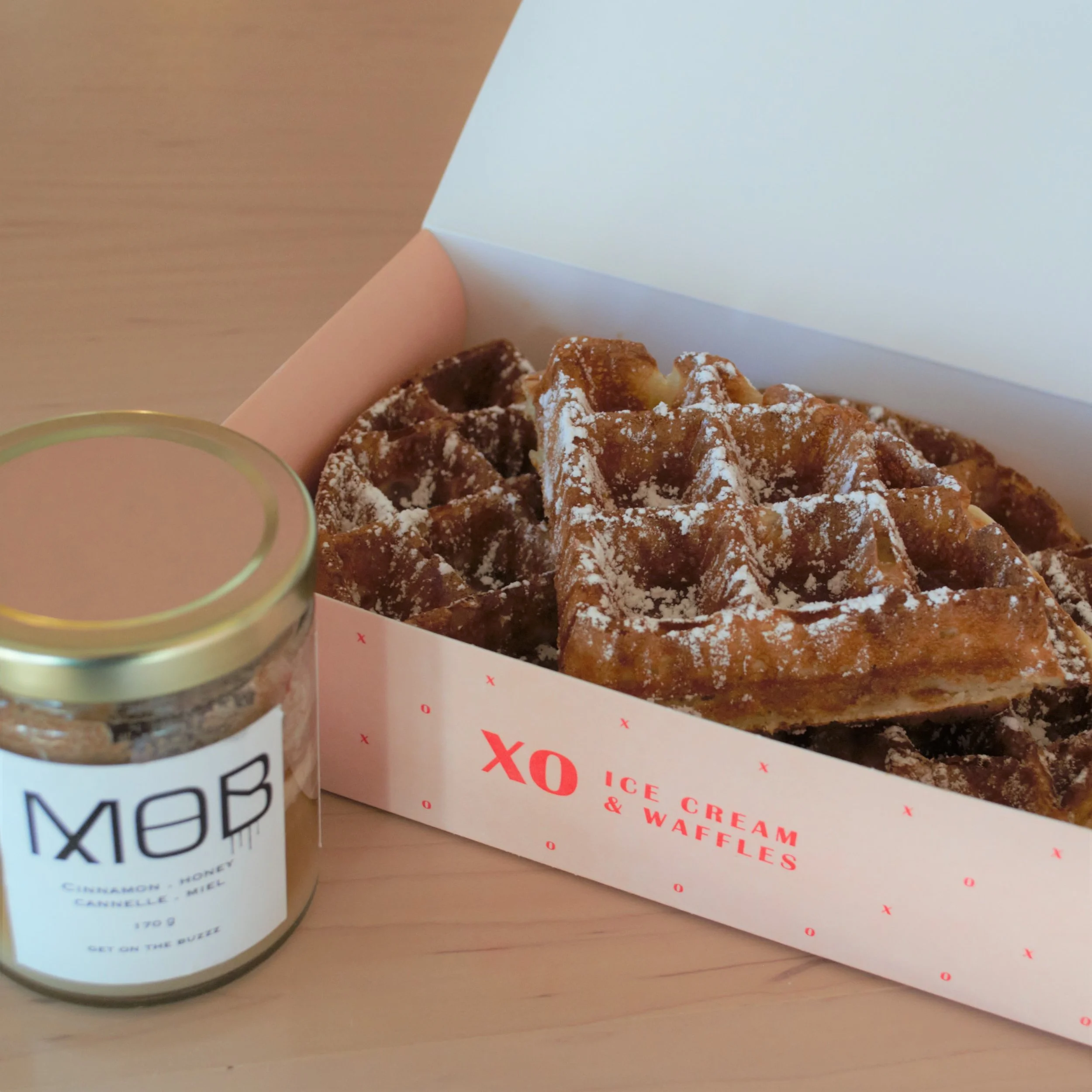 Waffle in a take away box, drizzled with cinnamon honey and jar of honey next to it