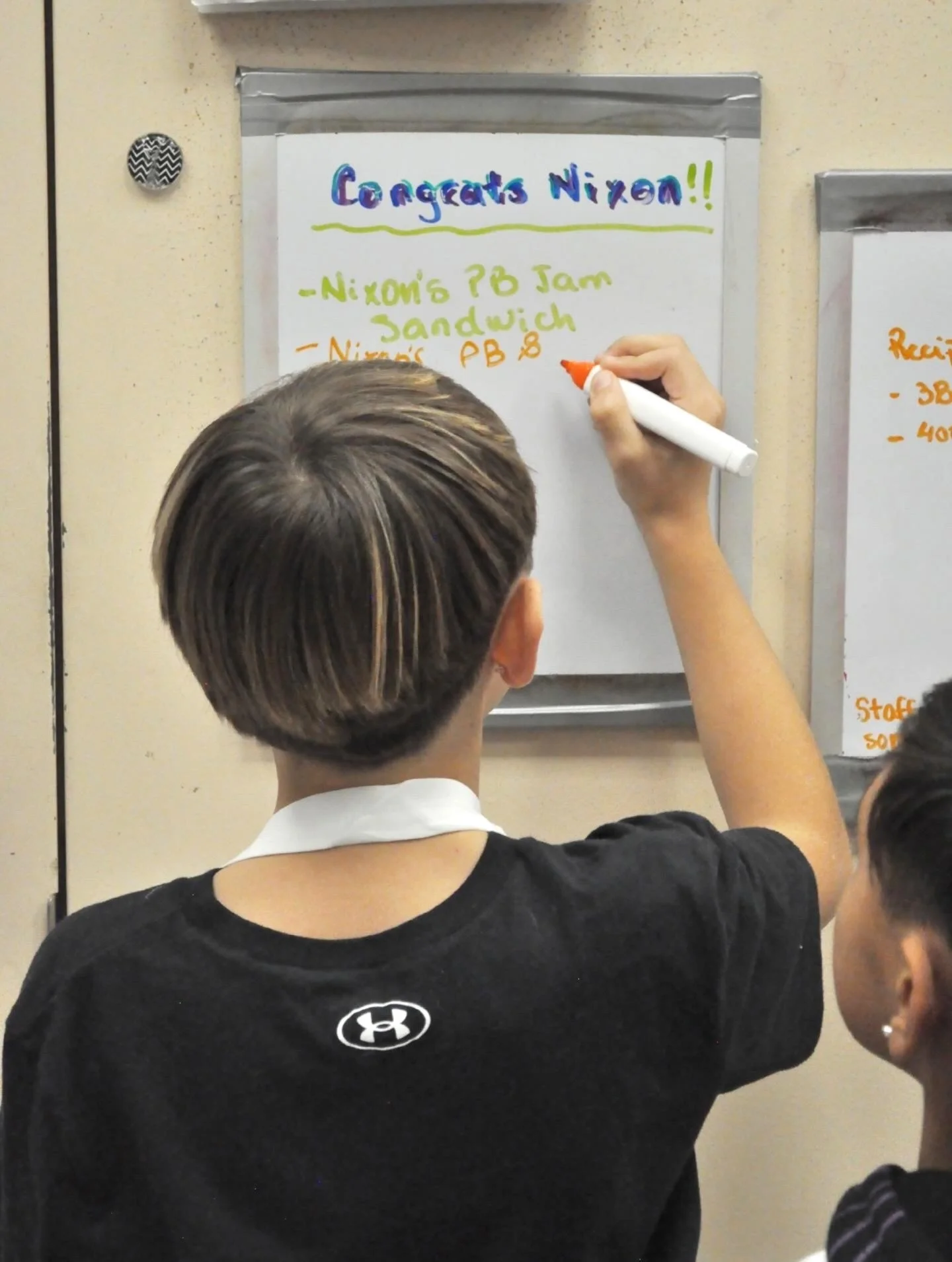 A child is writing the name of his ice cream on a whiteboard with a red marker.
