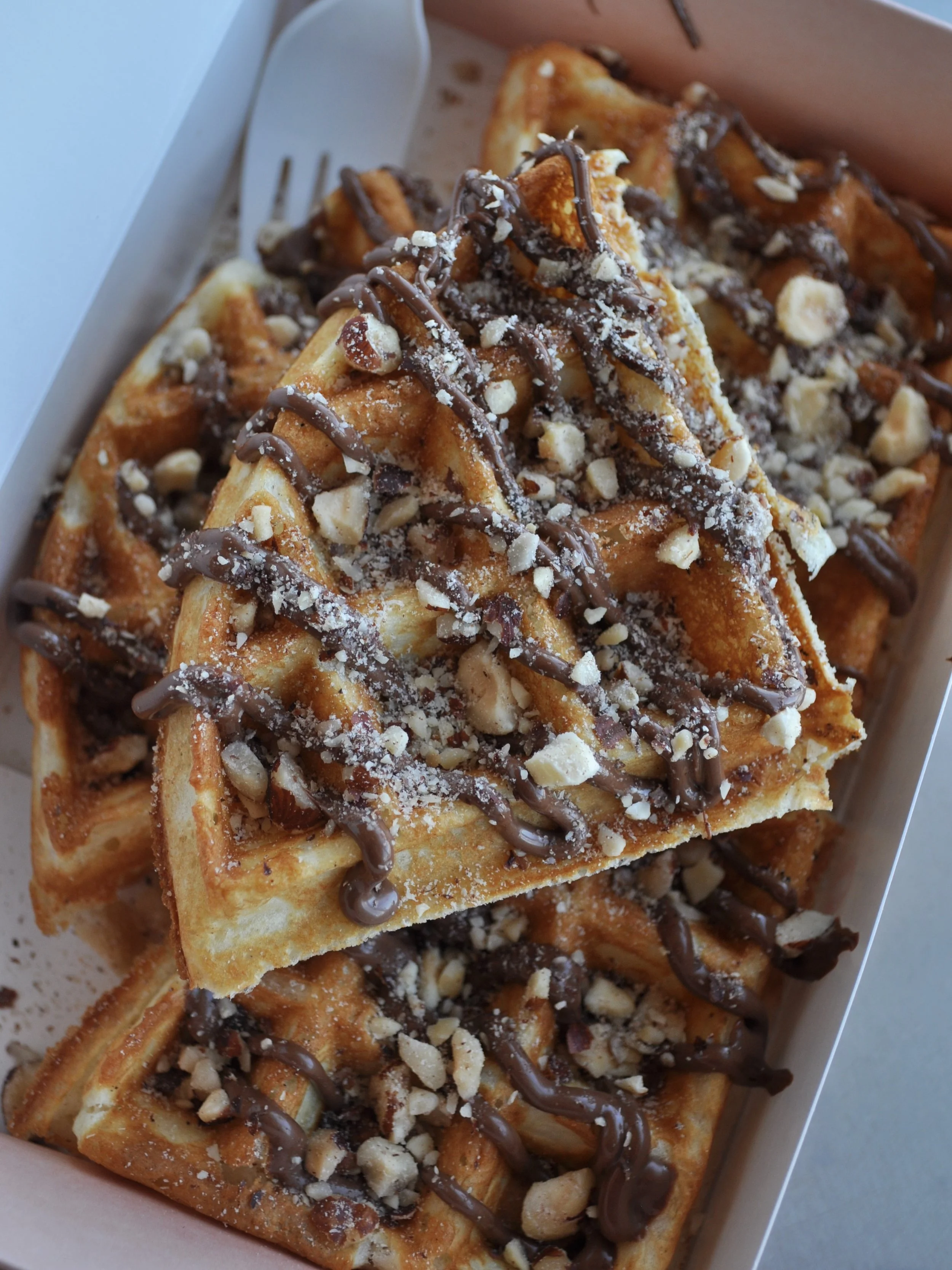 Slices of waffles covered in drizzle of nutella and crushed hazelnuts