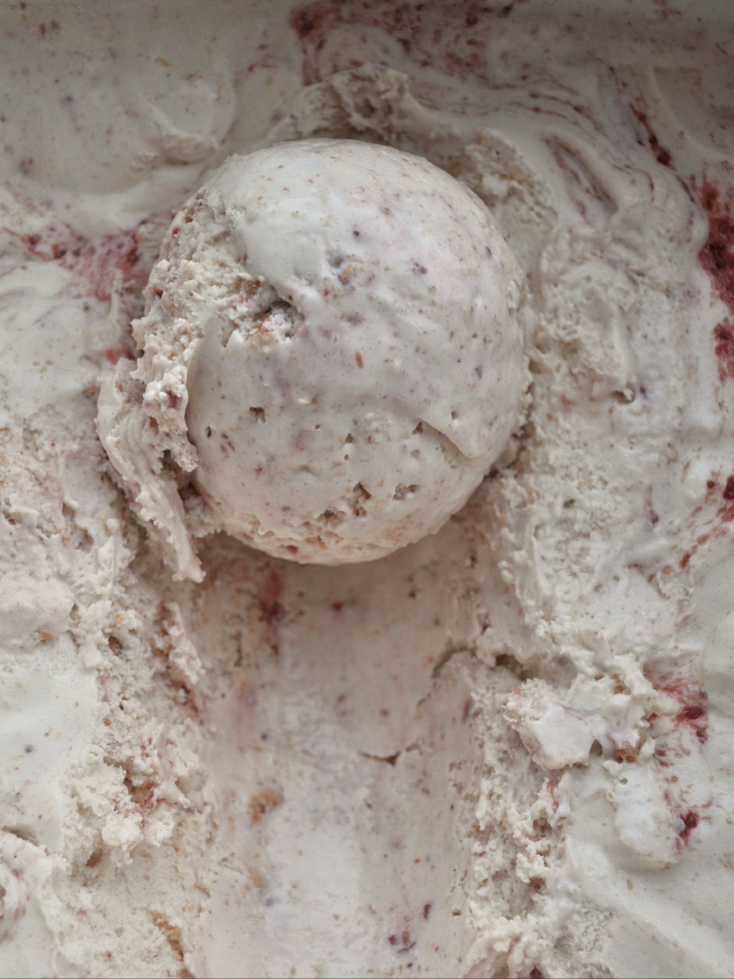 Close up of a scoop of Nixon's PB & Jam ice cream with peanut butter and swirls of strawberry jam in it. 