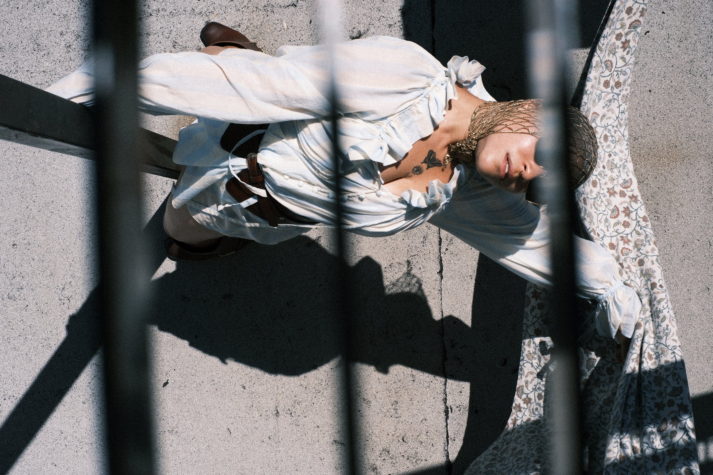 A woman lying on the ground next to a floral-patterned blanket, seen through black metal bars.