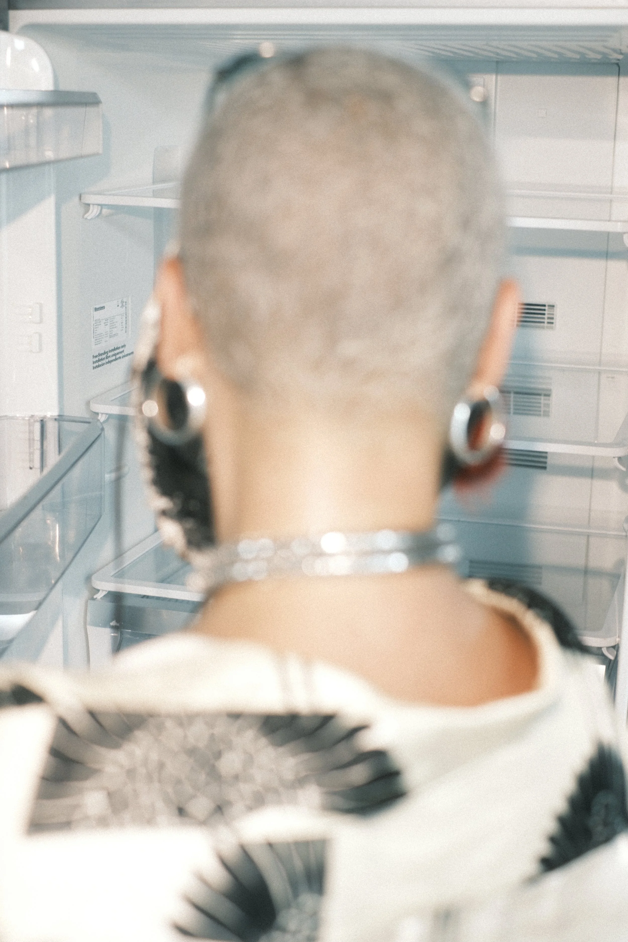 View inside a refrigerator looking at an overhead shelf and the back wall, with the top of a person's head visible in the foreground.