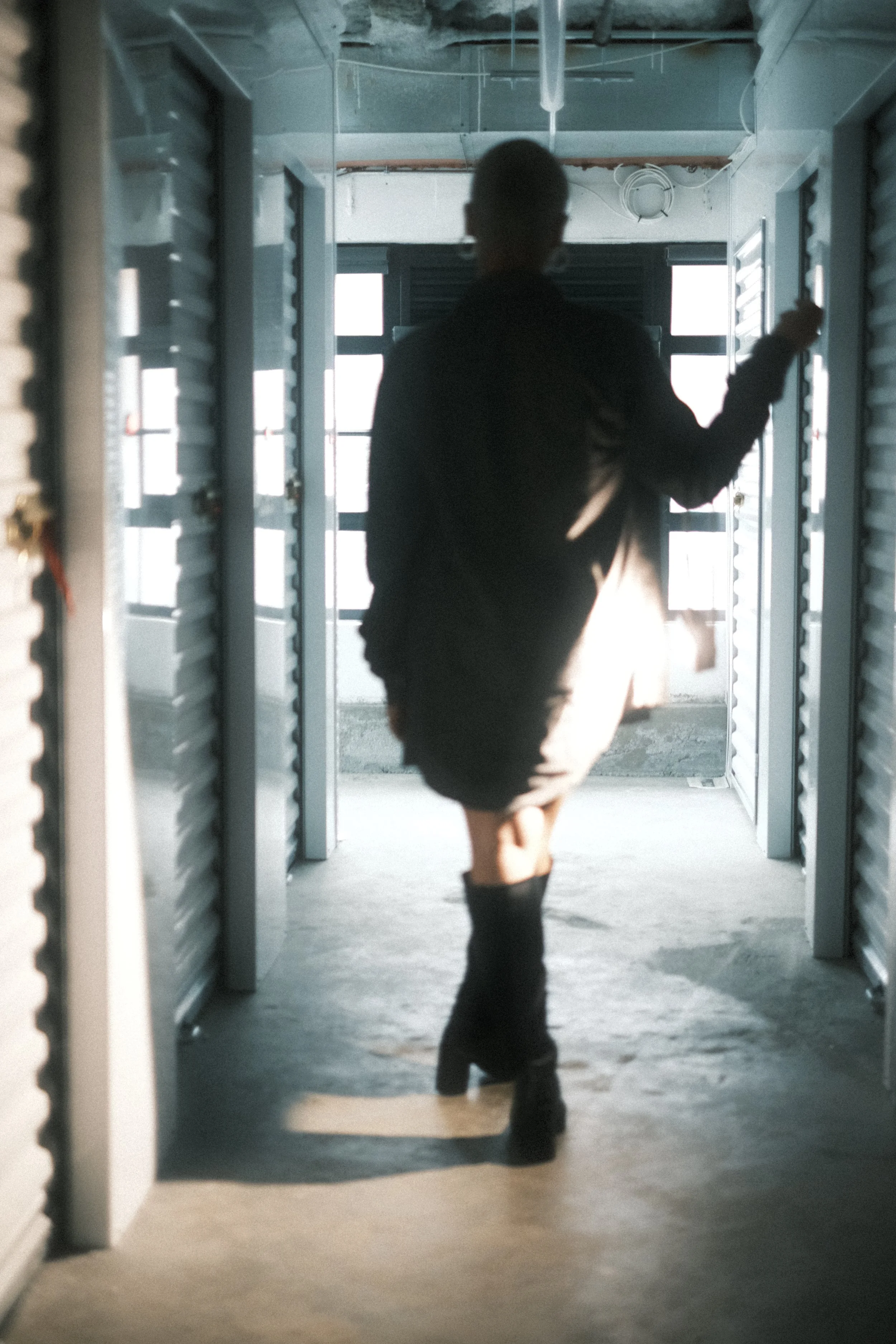 Silhouette of a person walking through a corridor, with bright light coming from open doors or windows on either side, creating a high contrast scene.