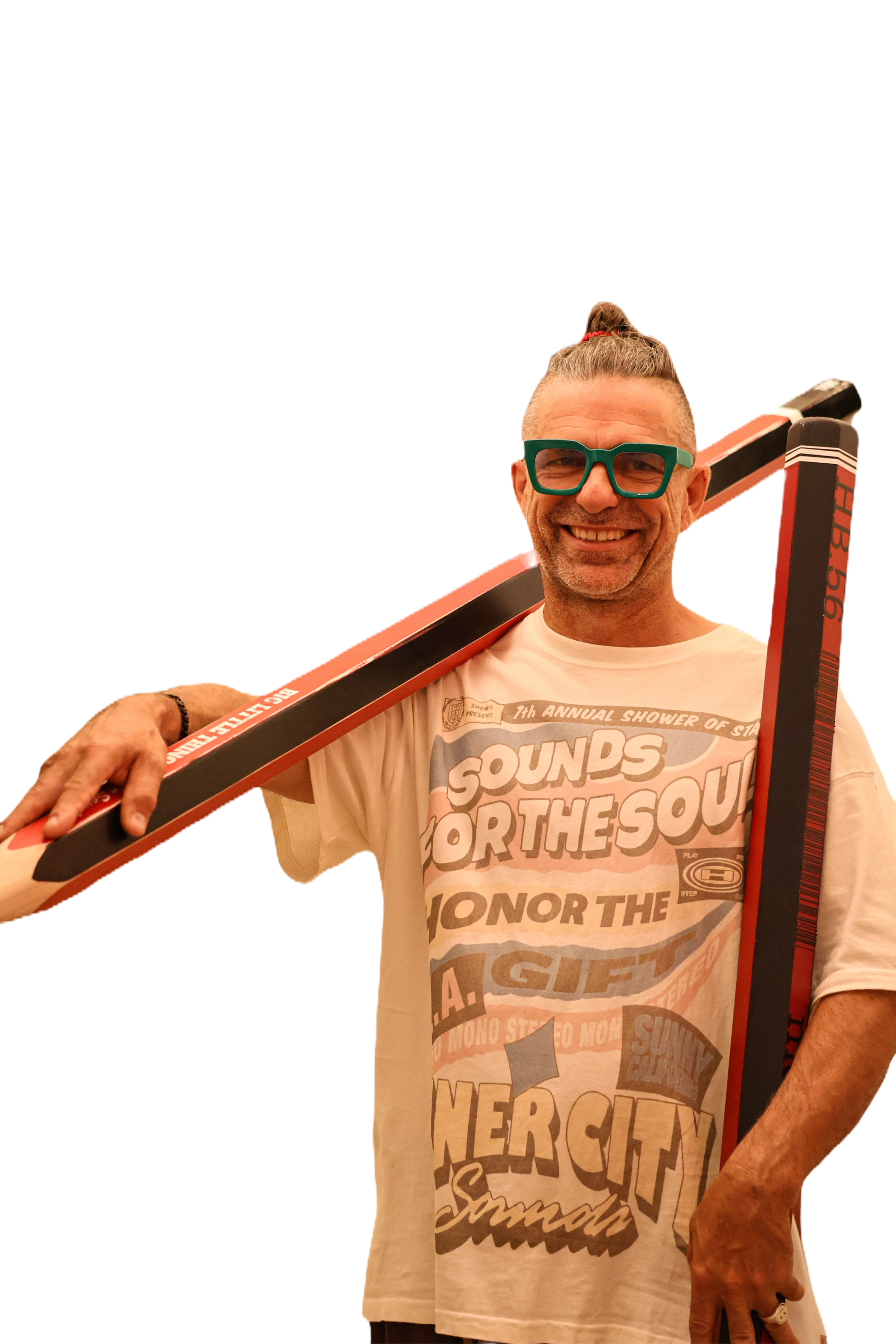 A man with glasses smiling, holding a surfboard over his shoulder, wearing a graphic t-shirt.
