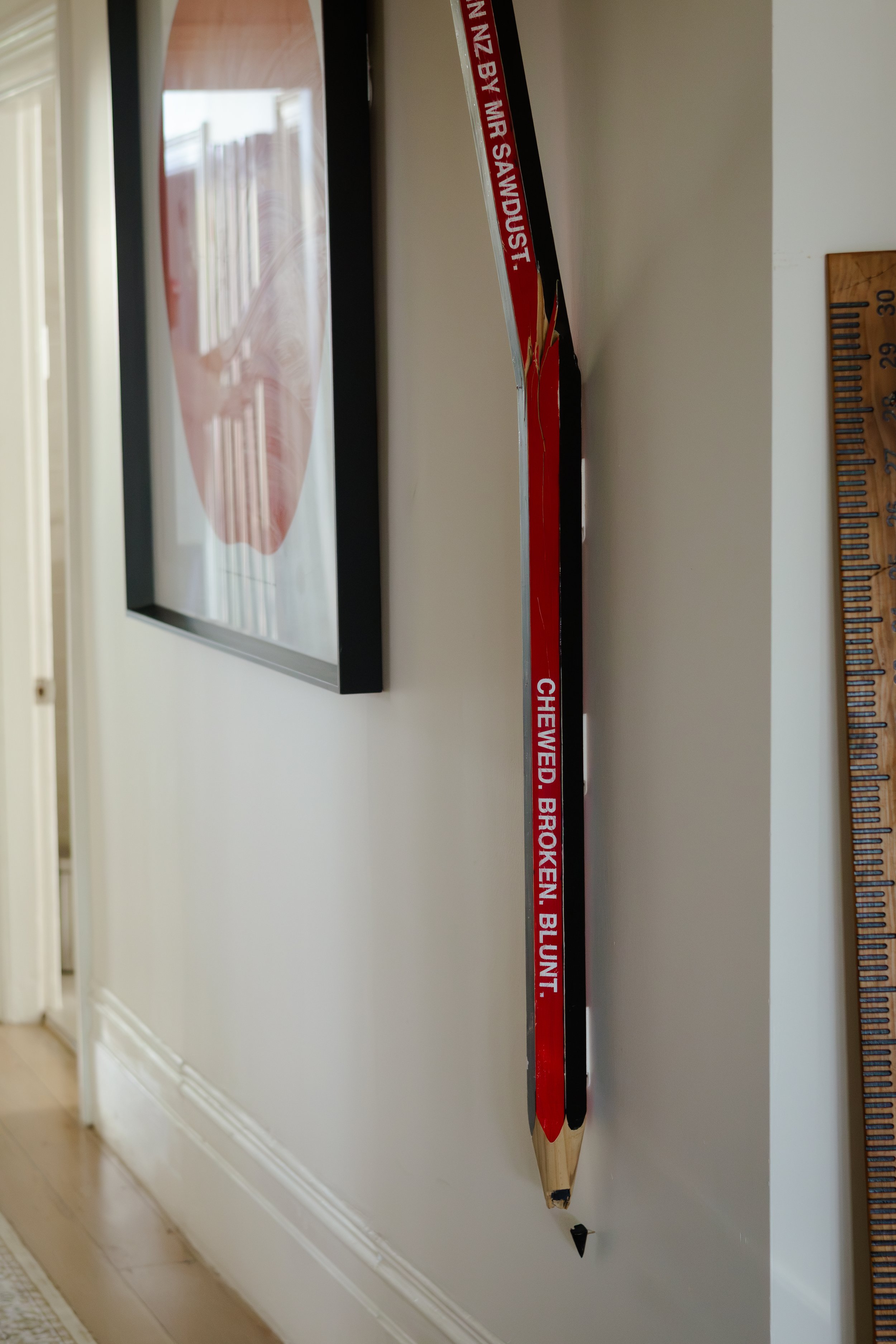A vintage wooden hockey stick mounted on a white wall, with a red and black design and the text 'CHEVRE, BROKEN BLUNT' visible on the stick.