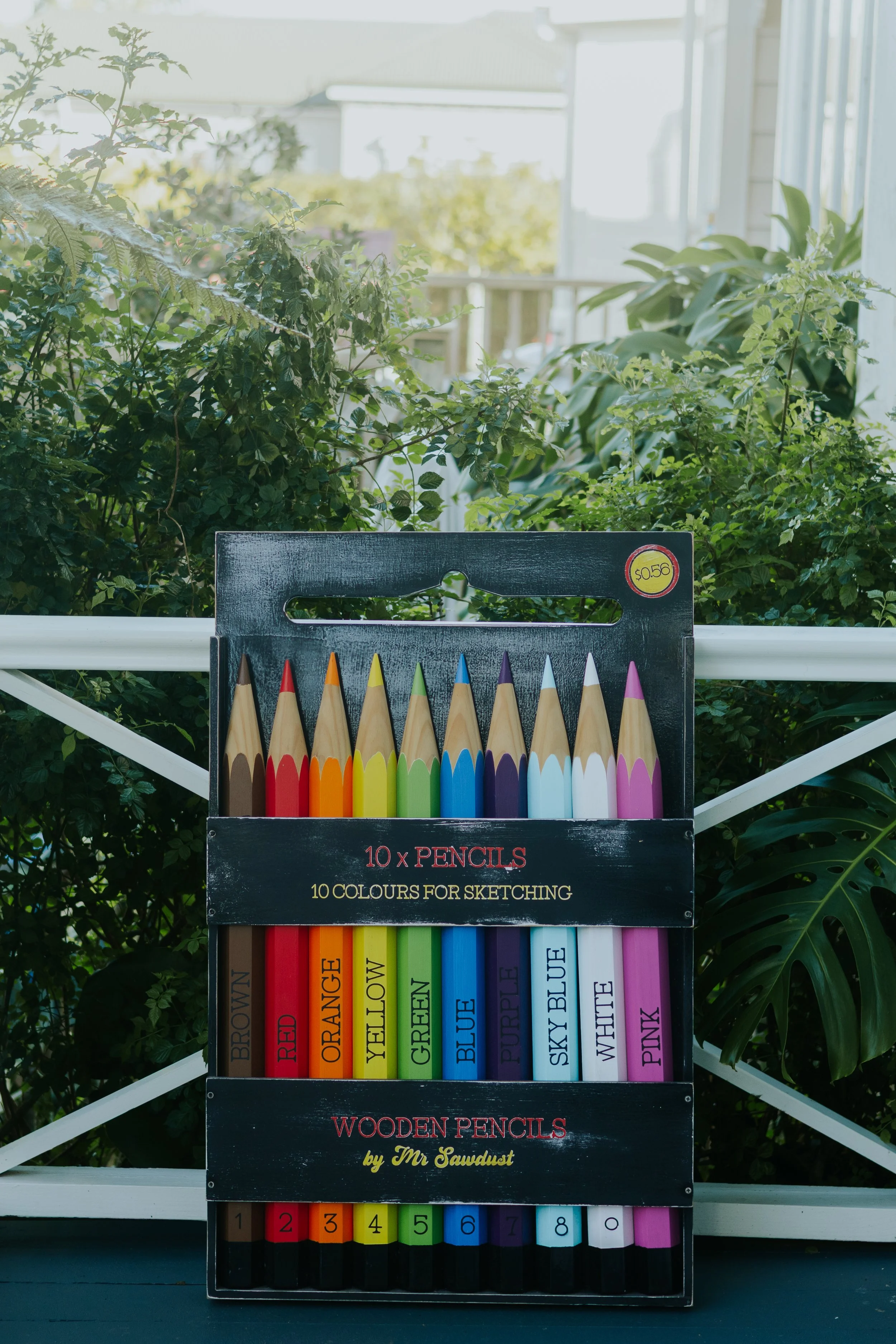 A set of colored pencils arranged in a black display box with labels for each color, including brown, red, orange, yellow, green, blue, purple, sky blue, white, pink, and black. The display box also has a label indicating it contains 10 colored penci