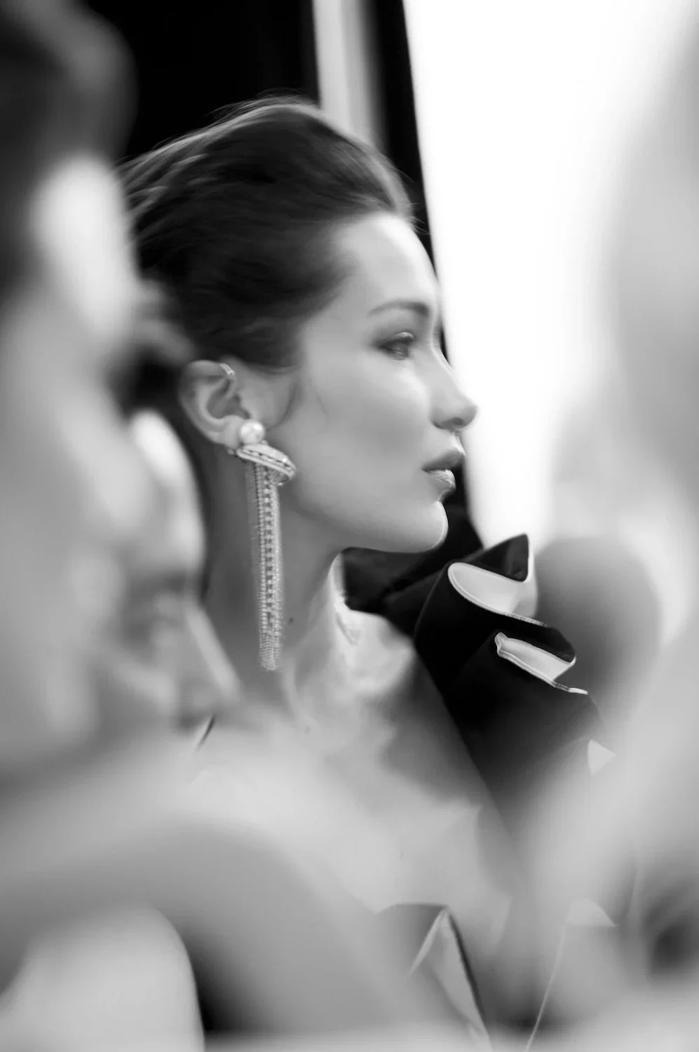 A woman with elegant earrings and styled hair, wearing formal attire, captured in profile at a formal event.