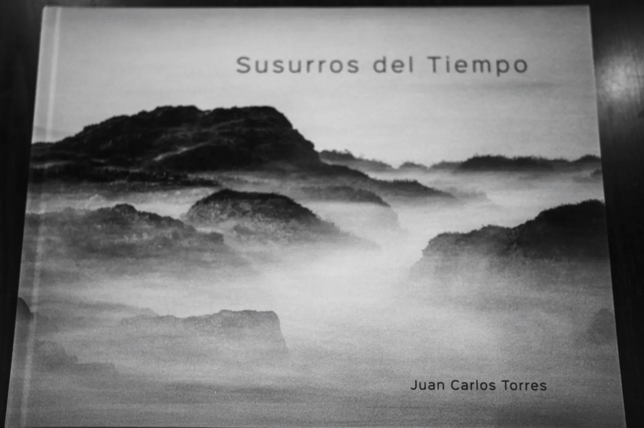A book titled 'Susurros del Tiempo' showing a landscape with fog-covered mountains and hills, with the author's name 'Juan Carlos Torres' at the bottom.