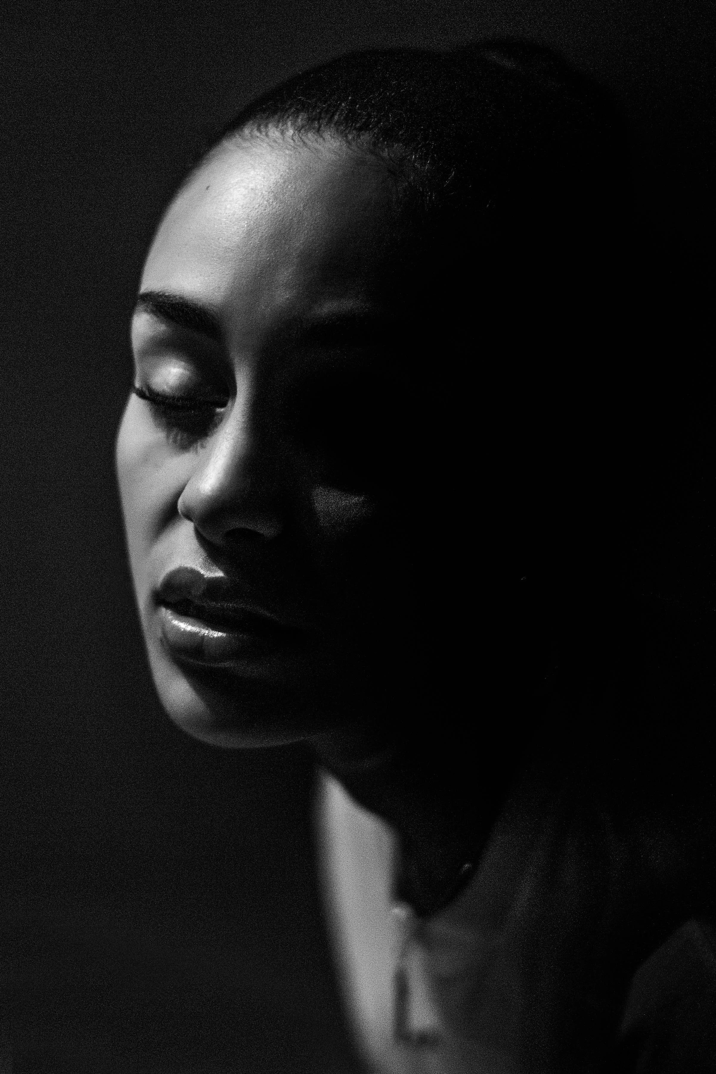 Close-up black and white photo of a woman's face with eyes closed, soft lighting highlighting her features, with shadows creating a dramatic effect.