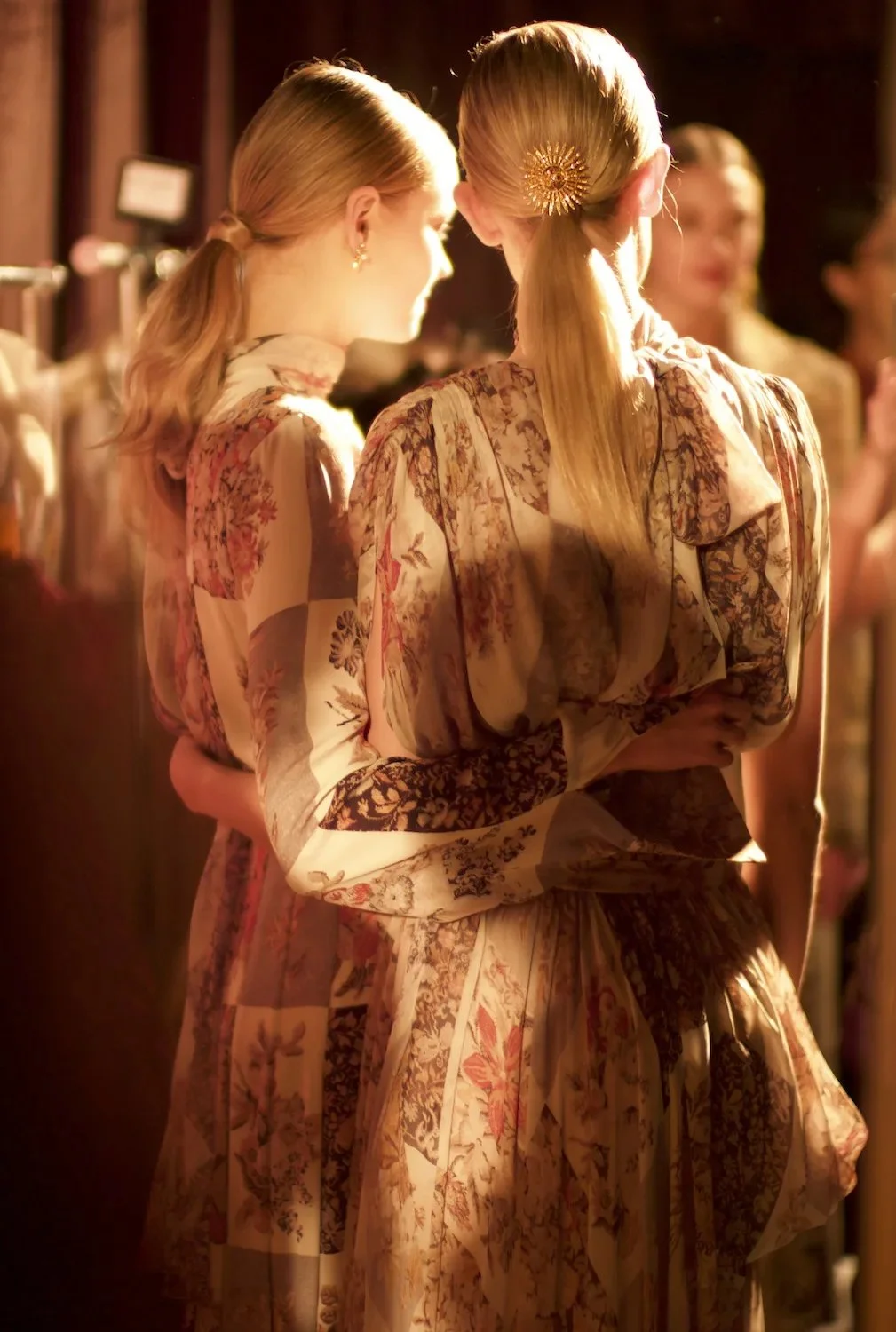 People dressed in vintage or floral patterned clothing, gathered in a warmly lit indoor setting.