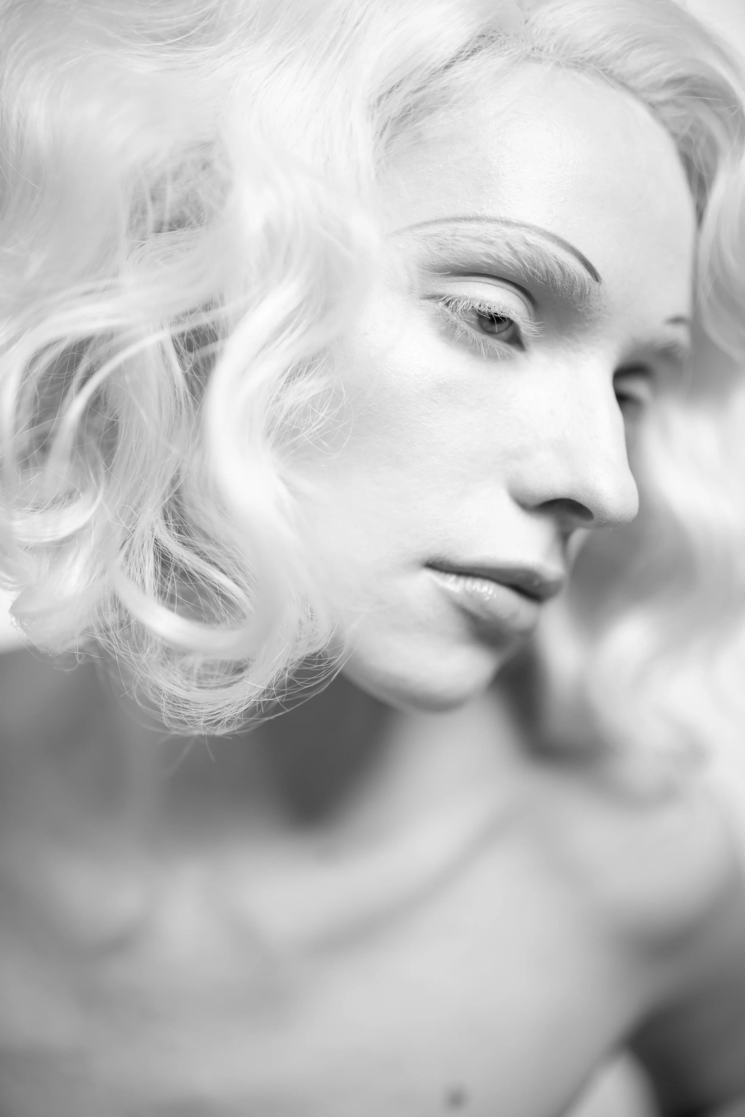 A black and white close-up photograph of a woman's face showing her eye, nose, and lips, with curly hair partially covering her face.