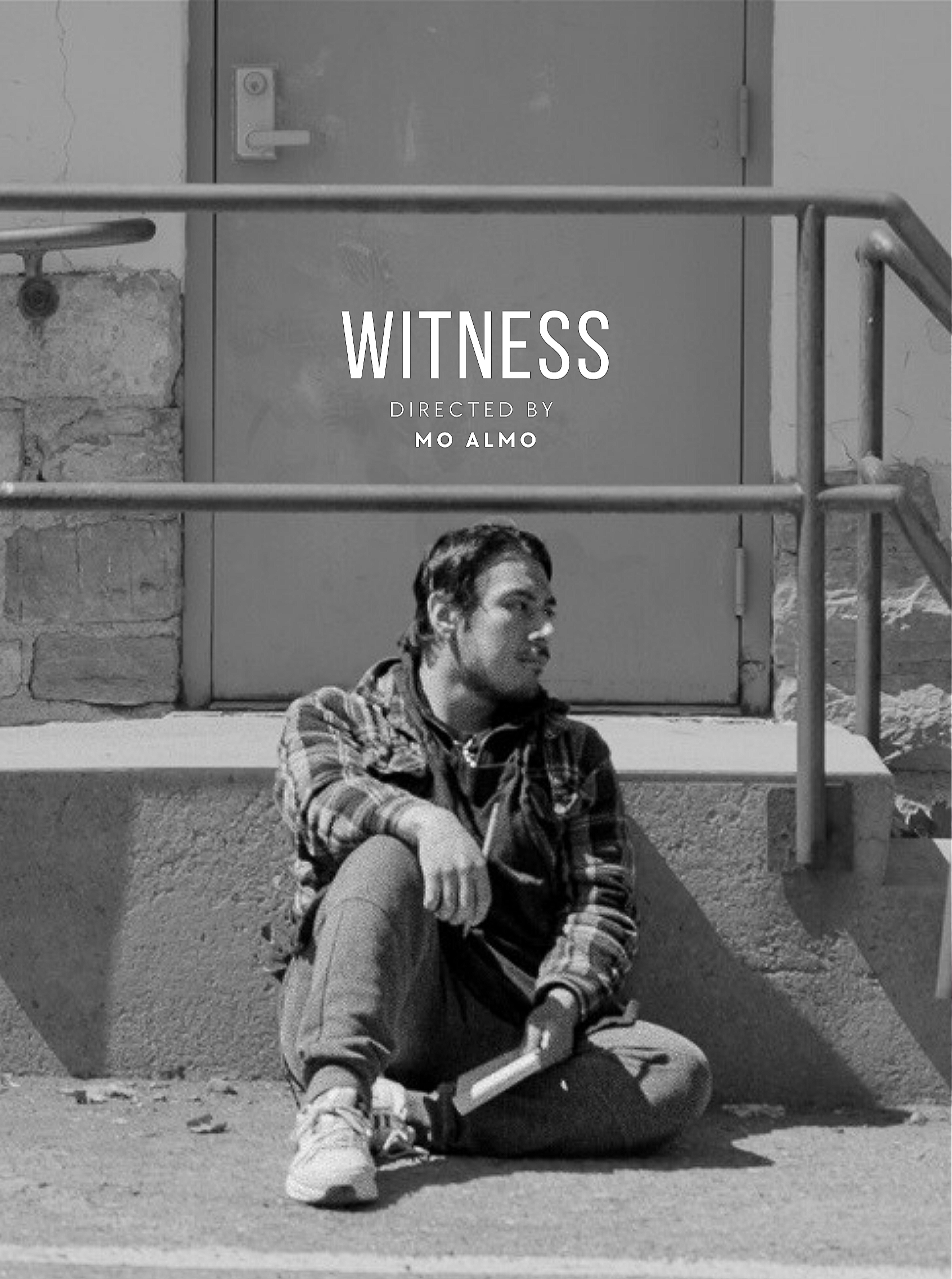 A black and white photo of a young man sitting on the sidewalk with a cigarette in one hand and a book in the other, leaning against a wall, with stairs and a door behind him.