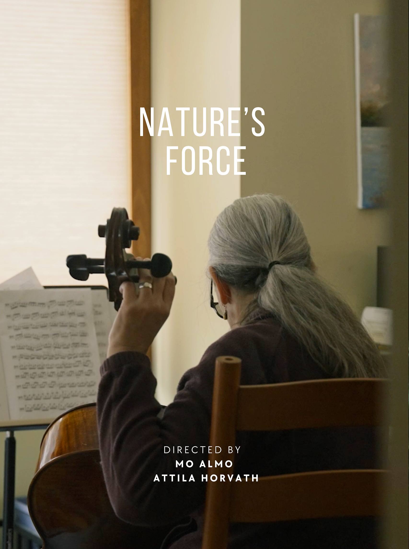 A woman with gray hair and glasses is playing a violin and reading sheet music in a room with beige and yellow walls, and artwork hanging on the wall.