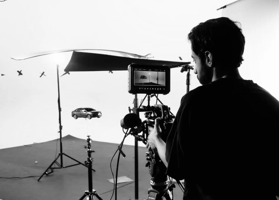 A person filming a car with a professional camera in a photo studio with a white background.