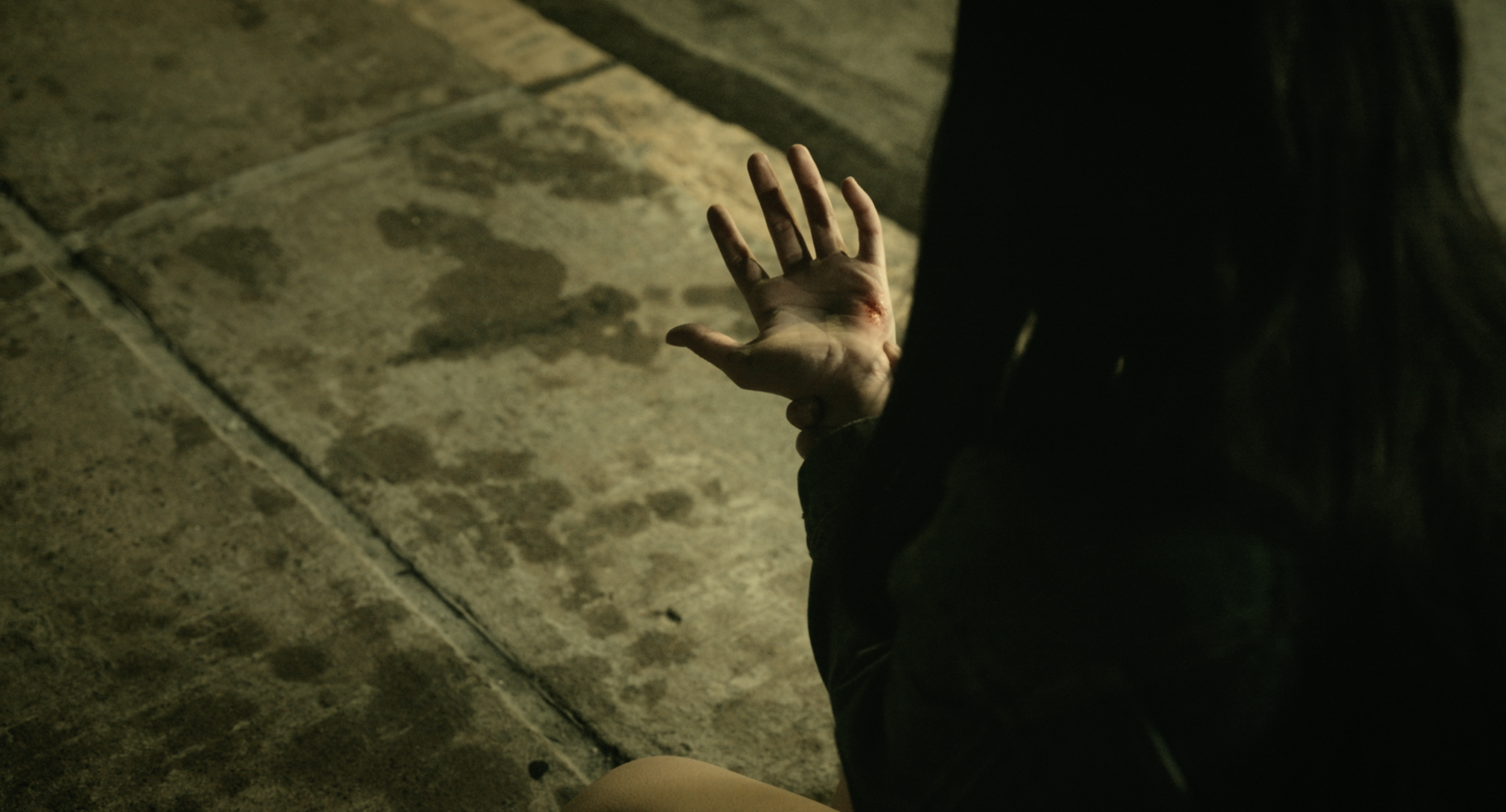 A person with a bloody hand and a visible wound on their finger, crouching on a stone surface at night.