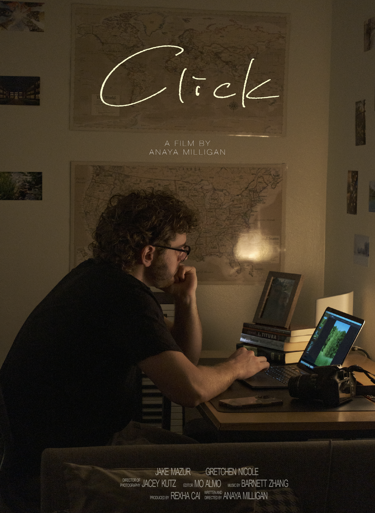 A person with curly hair and glasses sits at a desk with a laptop, books, and a small framed picture; a map of the world hangs on the wall behind, and a photo collage is on the wall to the right.