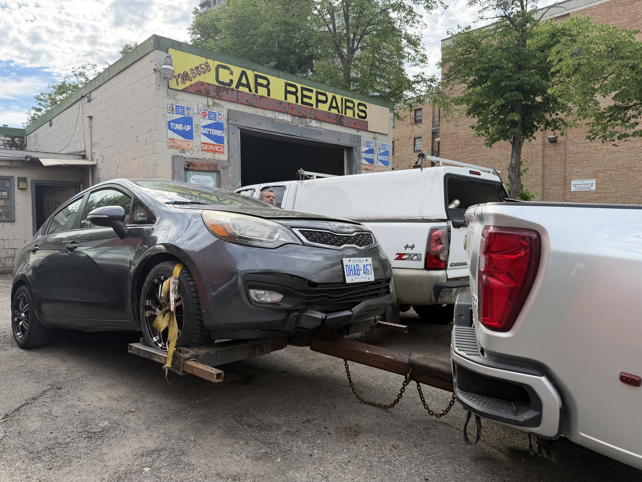 A car repair shop with a sign that reads 'Car Repairs' and several parked cars in front. One car is on a tow truck or flatbed.
