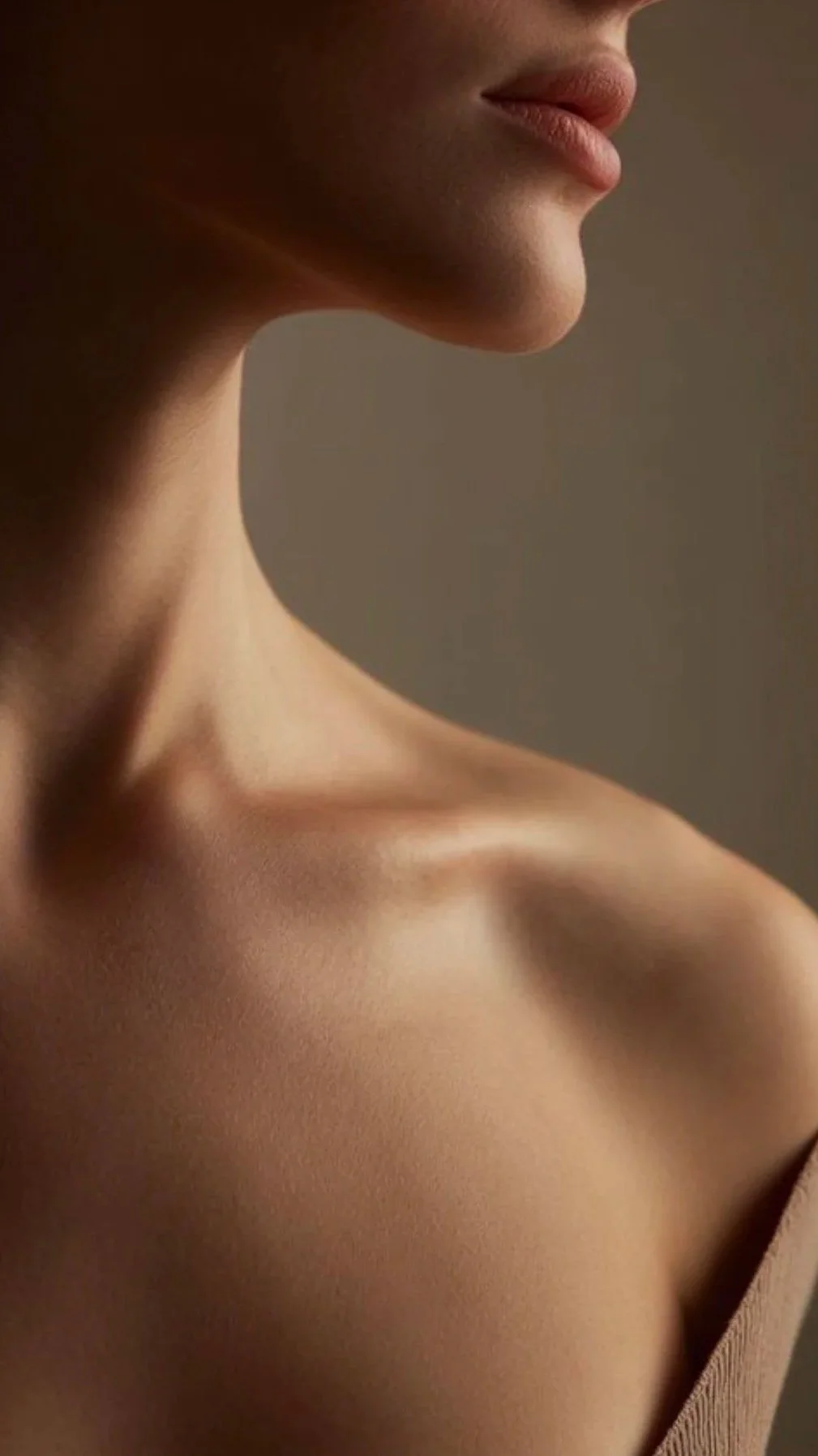 Close-up of a woman's chin, lips, and shoulder with smooth skin and soft lighting.