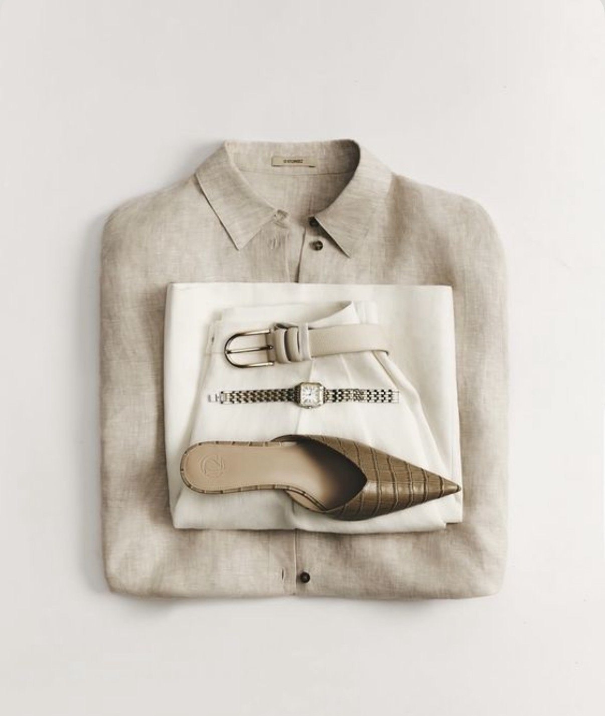Flat lay of beige shirt with white pants, beige belt, silver watch, brown checkered high heel, and silver buckle.