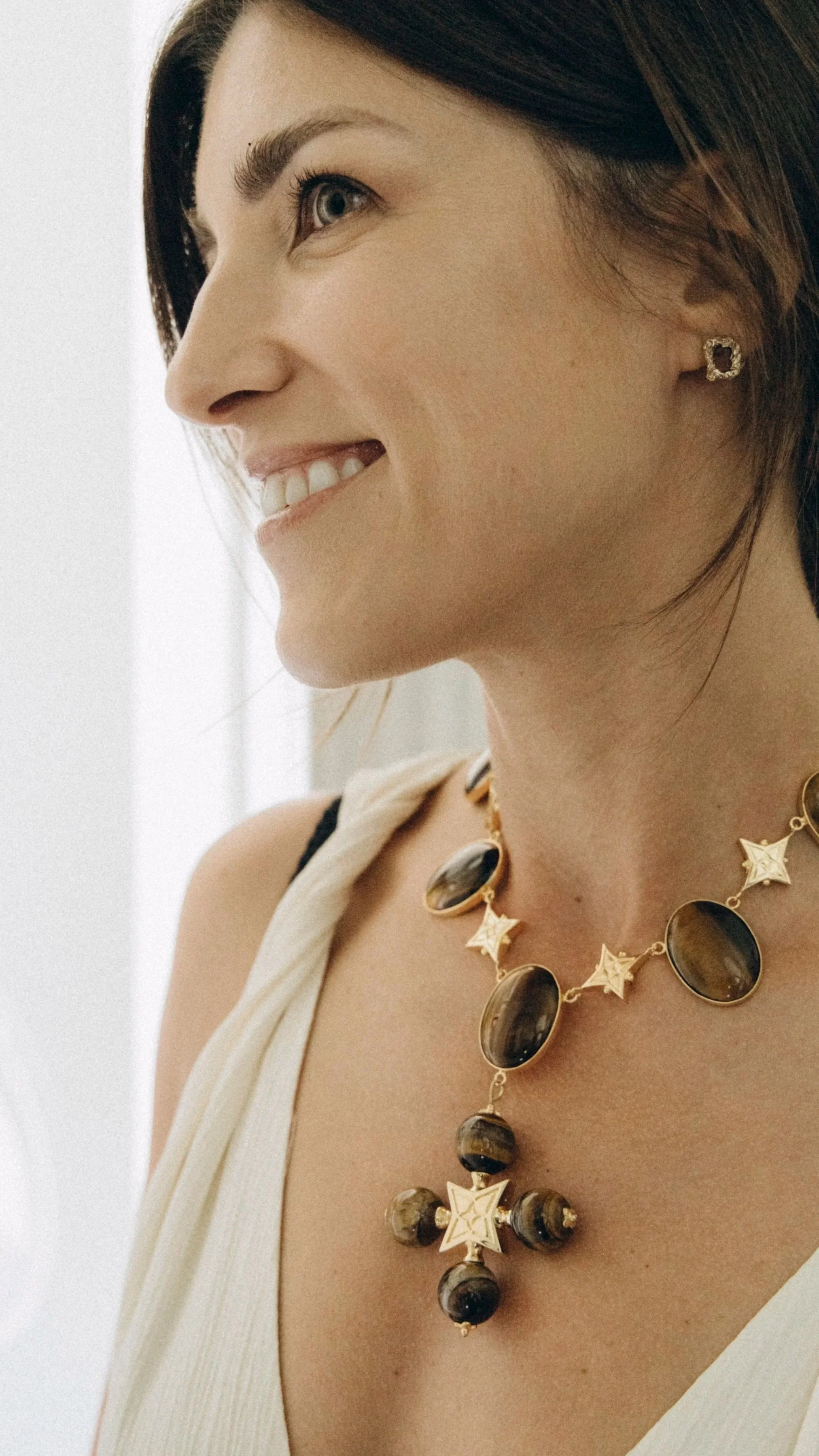 Close-up of a woman smiling, wearing a necklace and earrings.
