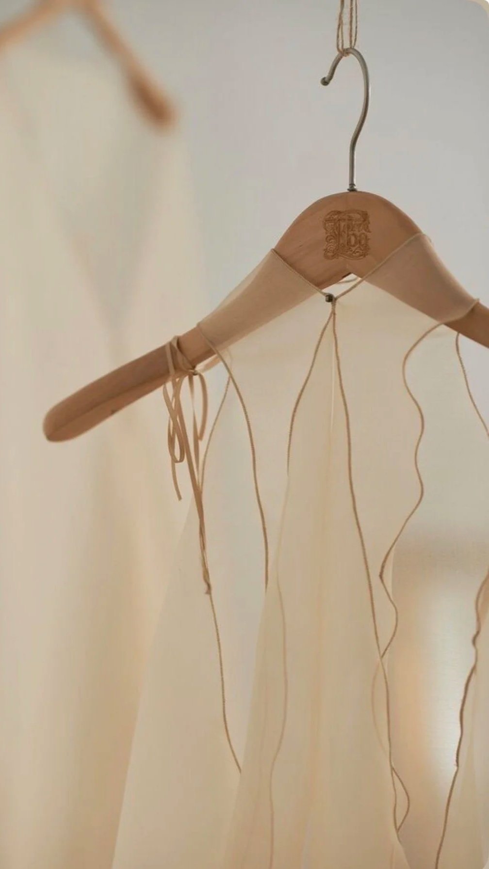 A wooden hanger with a decorative logo, hanging from a hook, with thin, curly, light-colored strips hanging down.