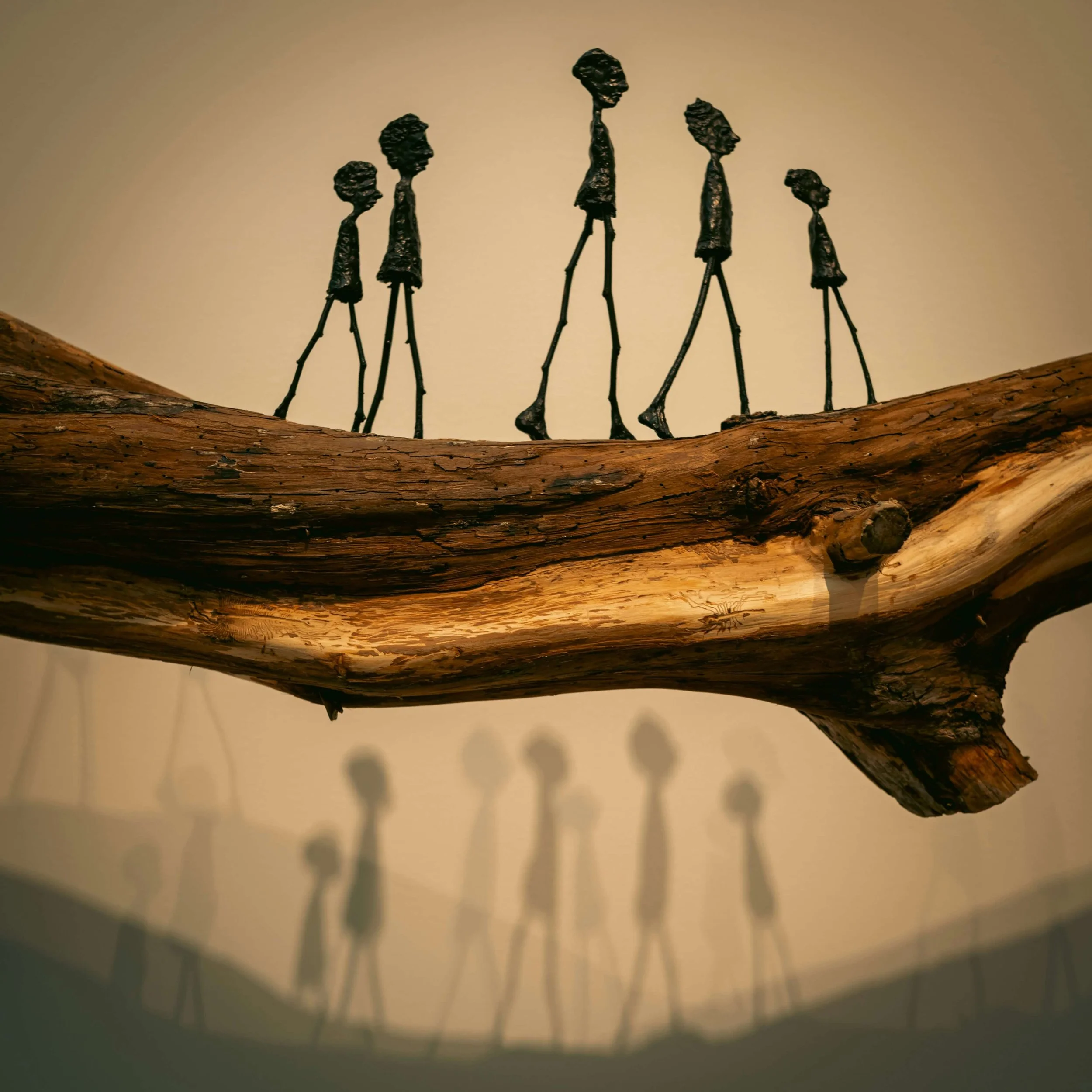 Artistic sculpture of human figures with elongated limbs and heads, standing on a piece of wood.