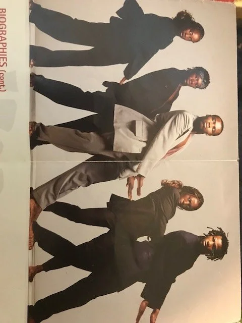 Five African dancers standing in a row doing a dance pose, dressed in formal attire, for a group photo.
