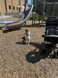 A young child playing with a toy in a playground area with a slide and a stroller.