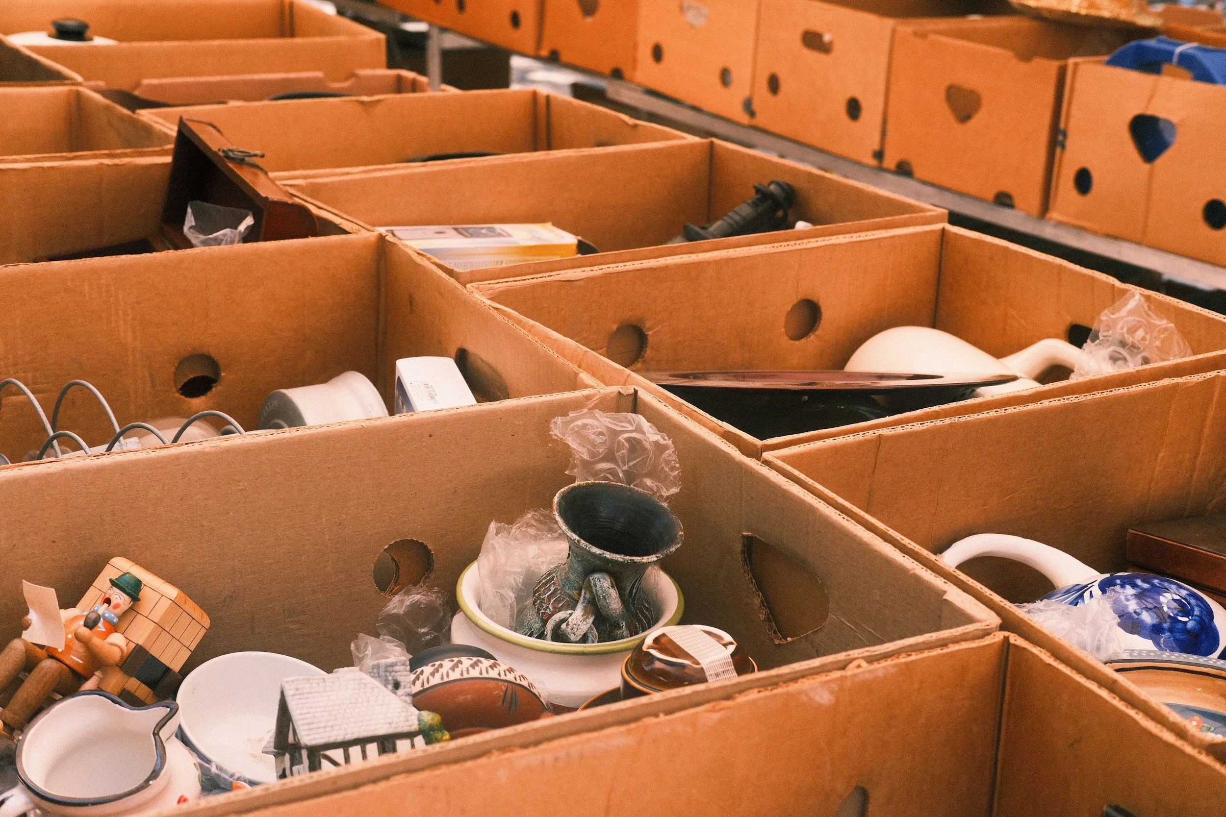 Boxes containing various household items and decorations, including ceramic figurines, bowls, and small appliances, stored on shelves.