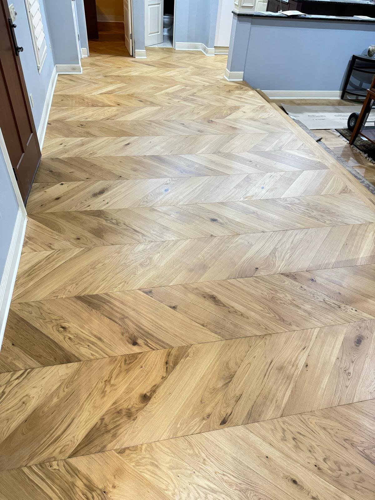 Interior view of a room with a newly installed light-colored wooden floor arranged in a herringbone pattern.