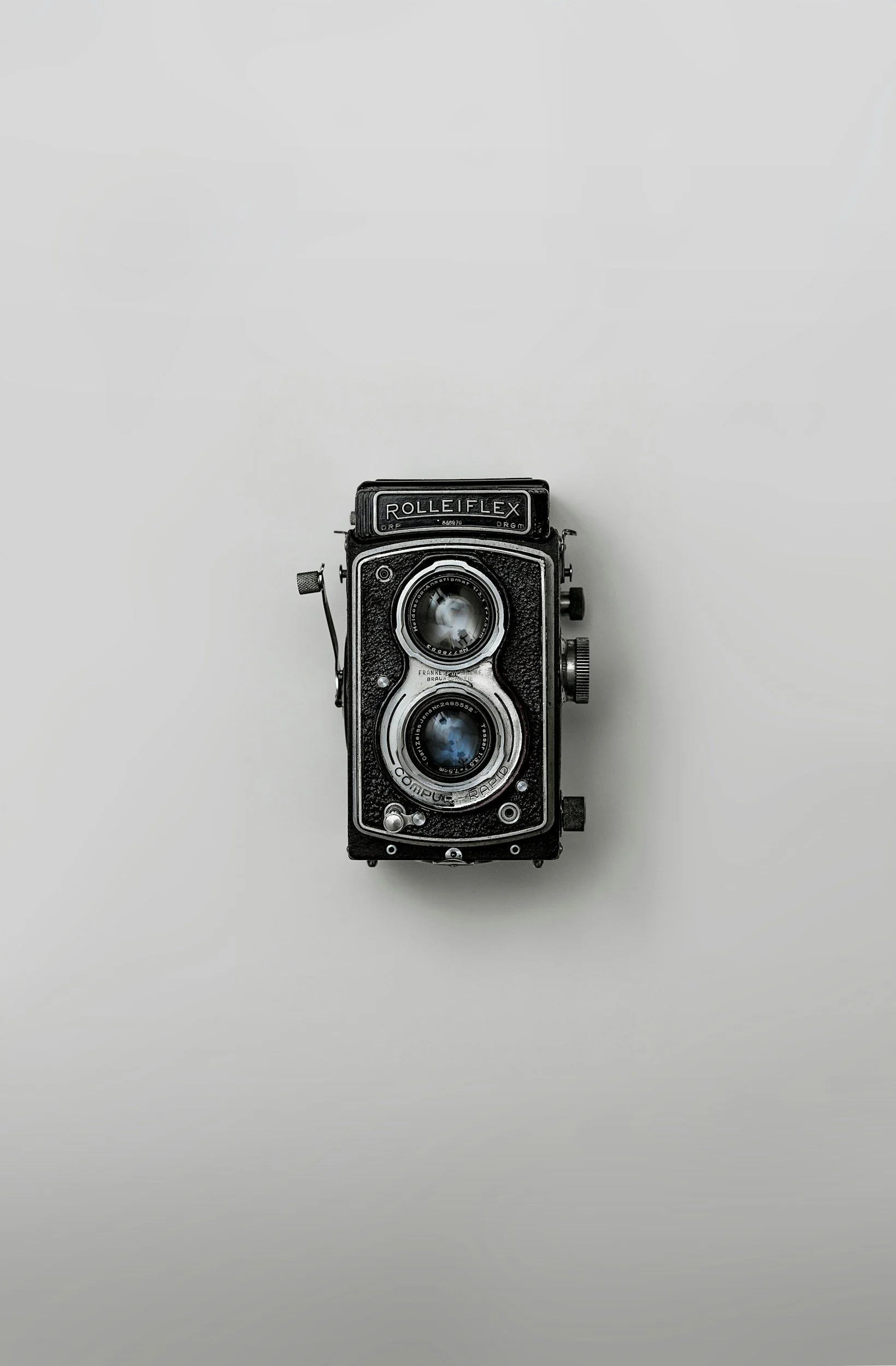 A vintage twin-lens reflex camera labeled 'RolleiFlex' is placed on a plain white surface.