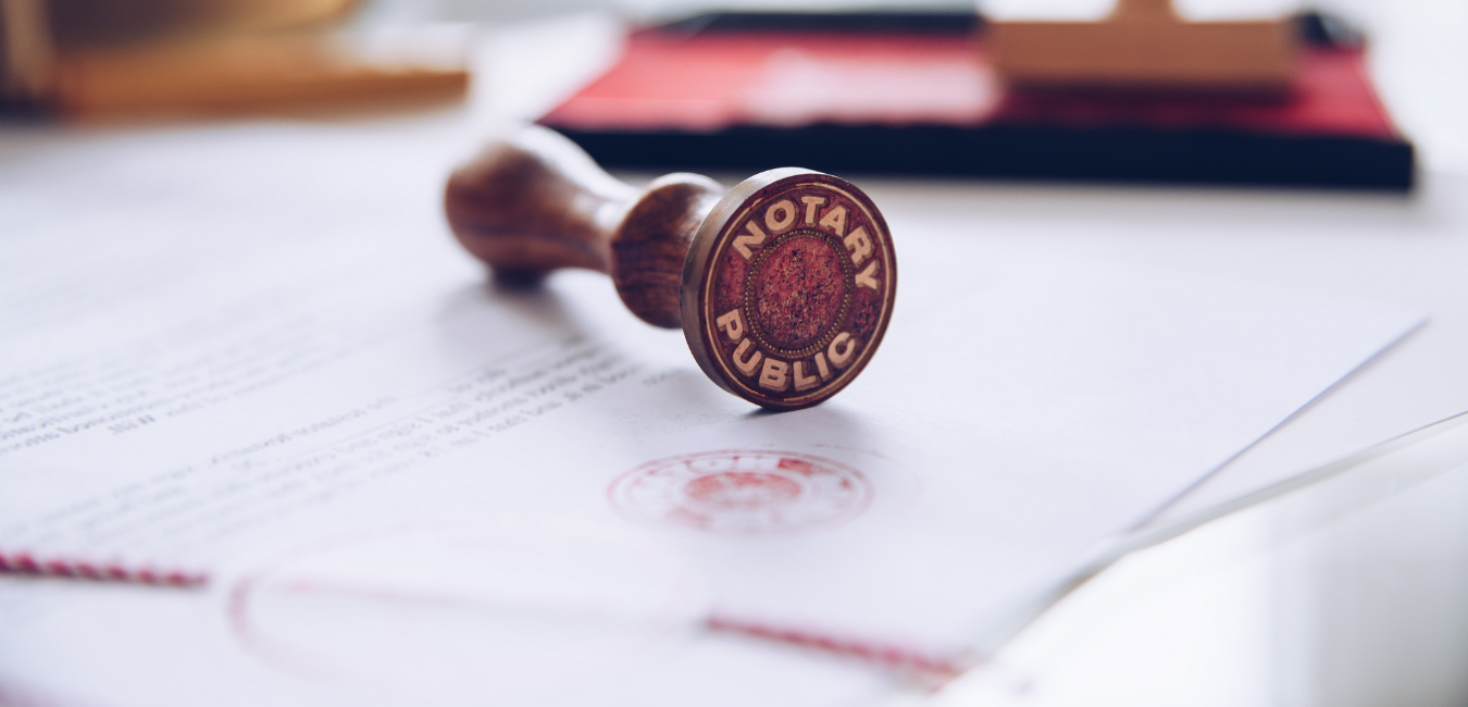 A wooden stamp with the words 'NOTARY PUBLIC' stamped on an official document and its red inked impression visible on the paper.