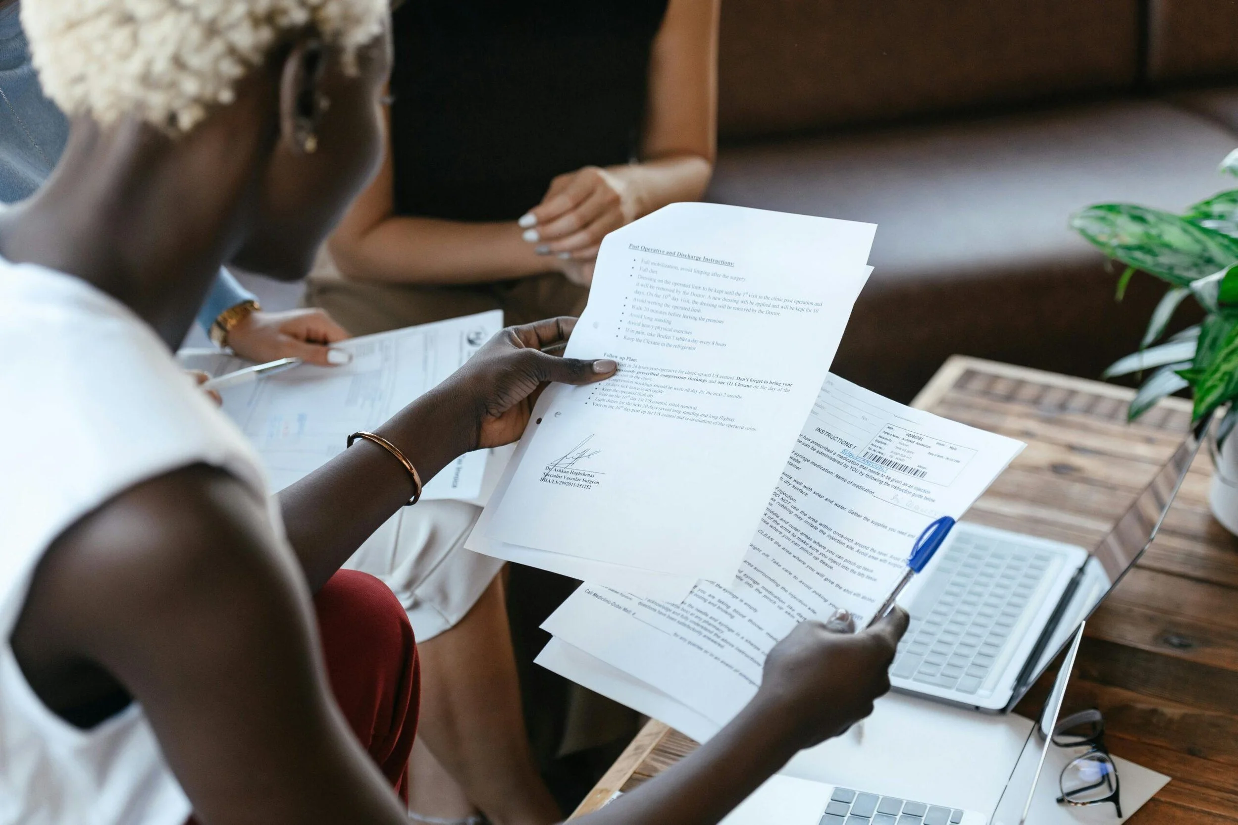 People sitting at a table reviewing documents, with a laptop and a plant nearby.