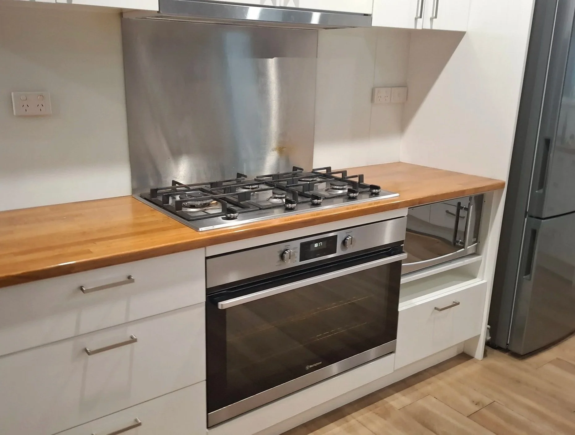 Modern kitchen with white cabinets, wooden countertop, stainless steel gas stove, oven, and refrigerator.