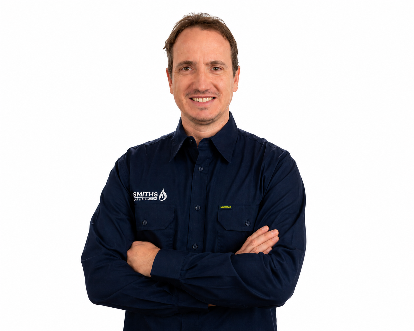 A man wearing a navy blue work shirt with embroidered logo and text, standing with arms crossed and smiling against a plain white background.