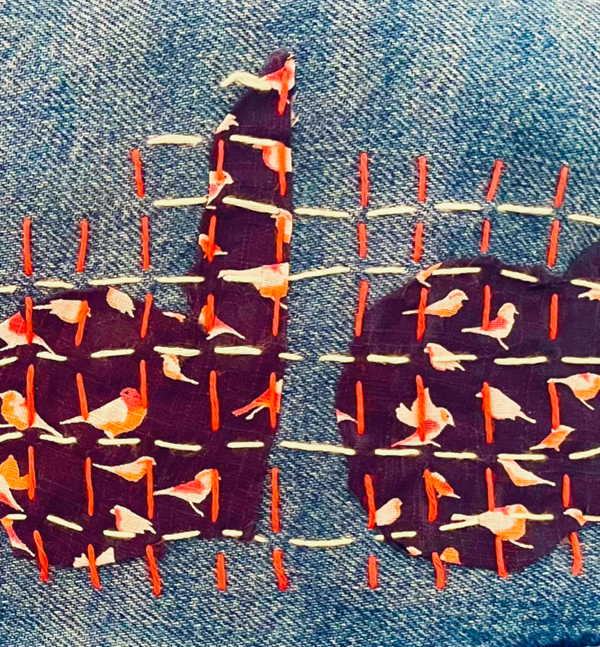 Embroidery of a heart with a pattern of small birds and orange stitches, placed on denim fabric.