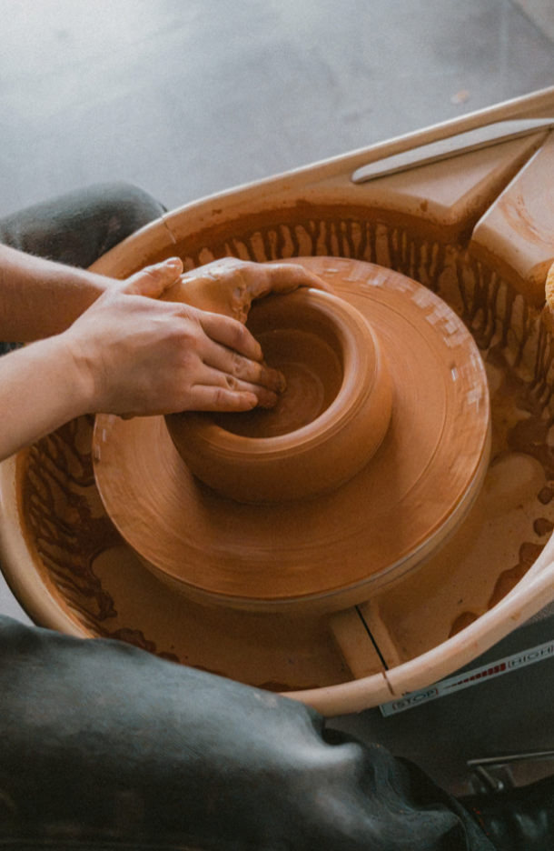 Close-up of a person shaping a clay pot on a pottery wheel in a pottery studio.