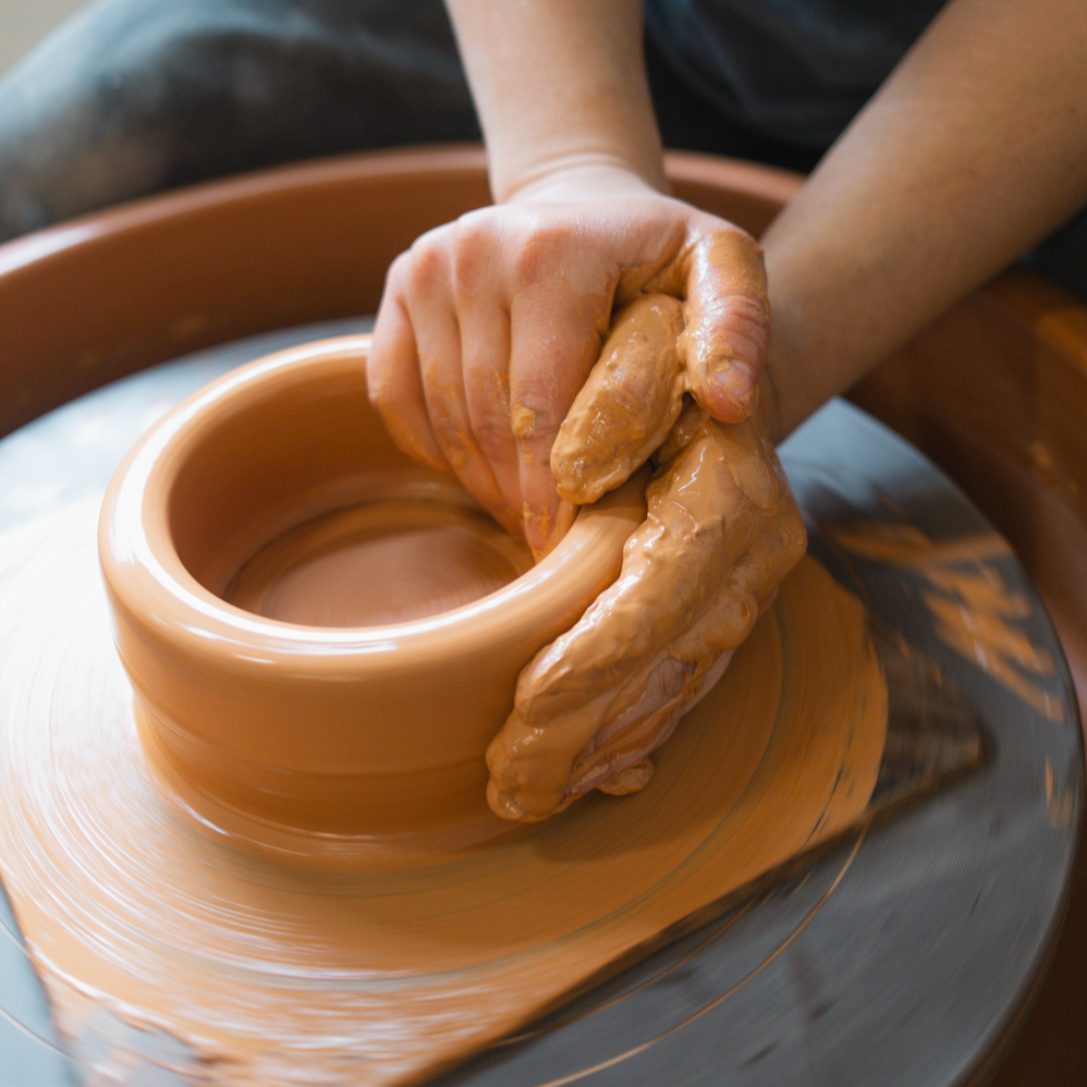 Person shaping clay on a pottery wheel with their hands.